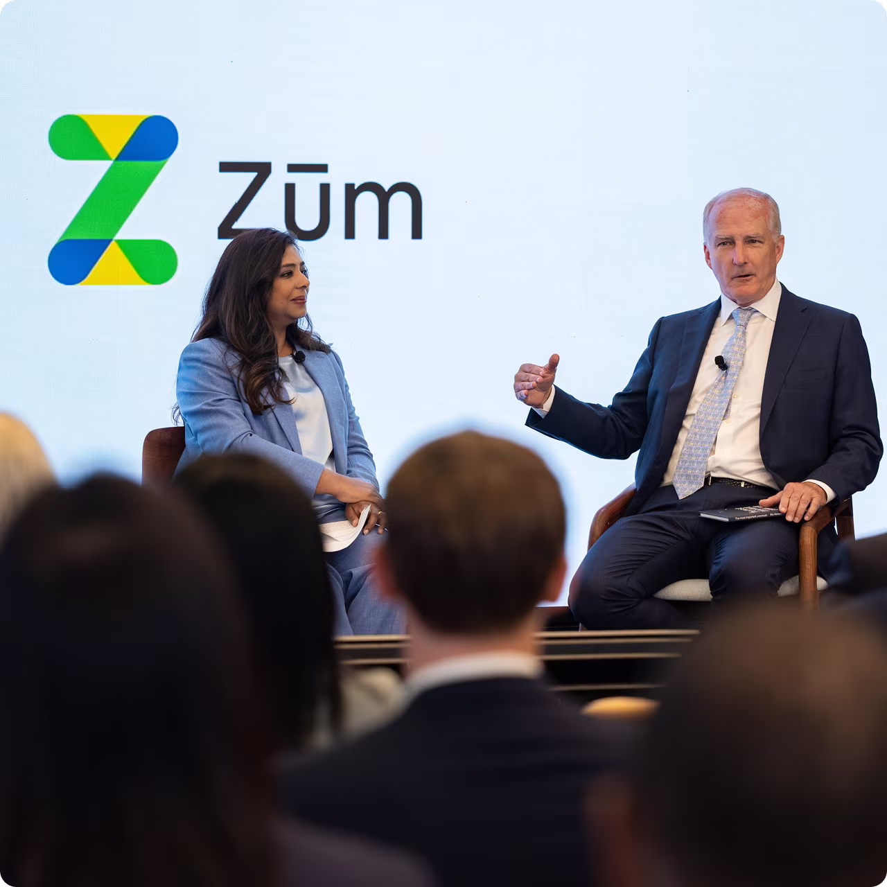 Two speakers at a Zum. event discussing school transportation solutions with the company logo