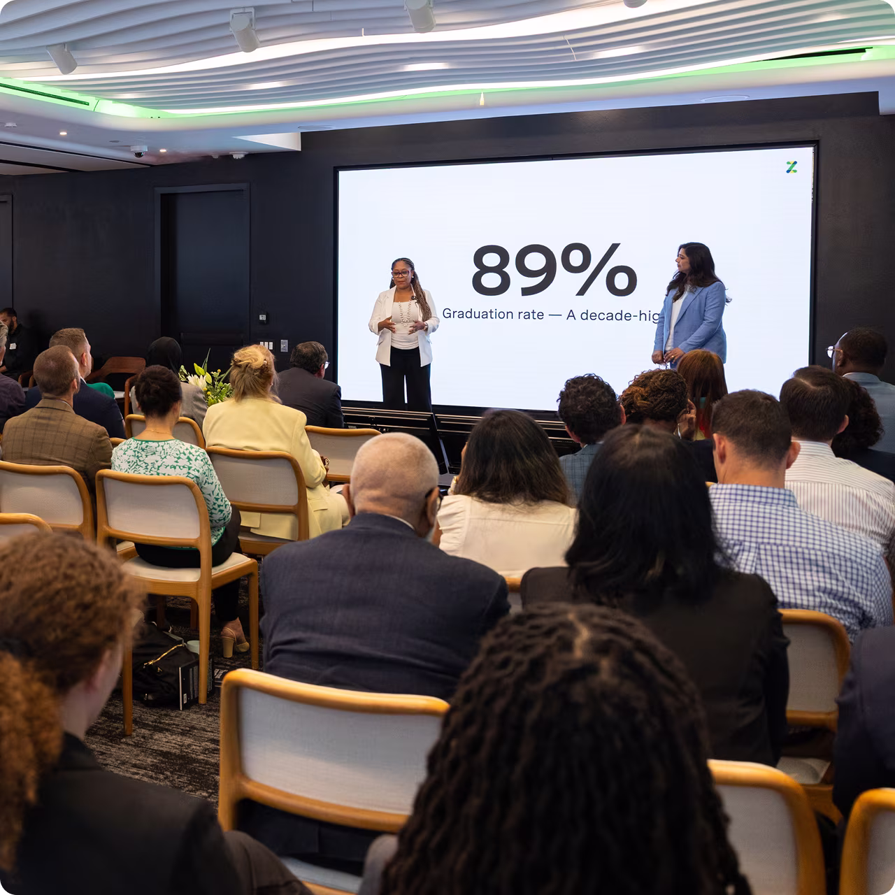 Presentation at Zum event showing a slide with 89% graduation rate and audience attentively