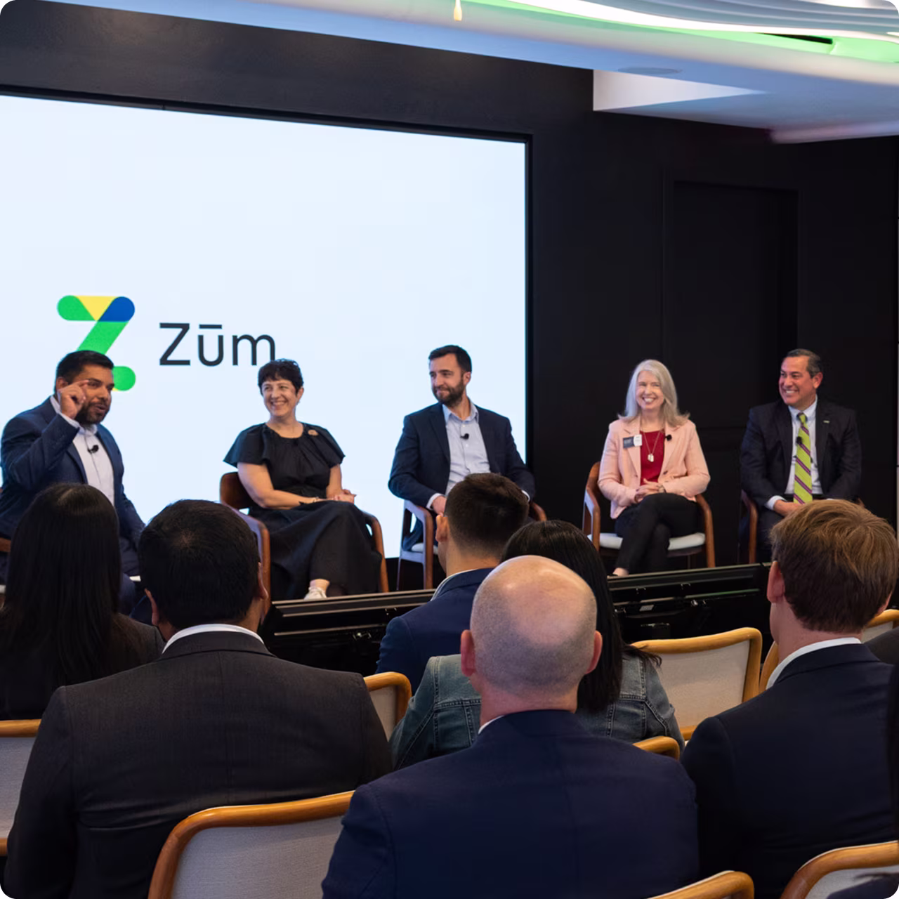 Panel discussion featuring five speakers in front of a Zum. logo, with an audience visible below.