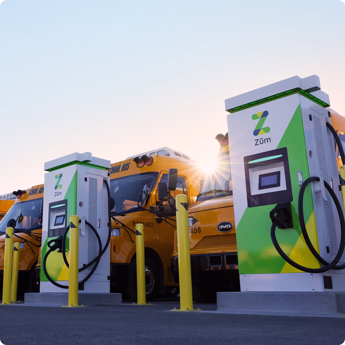 Two electric vehicle chargers with yellow school buses in the background at a charging station.