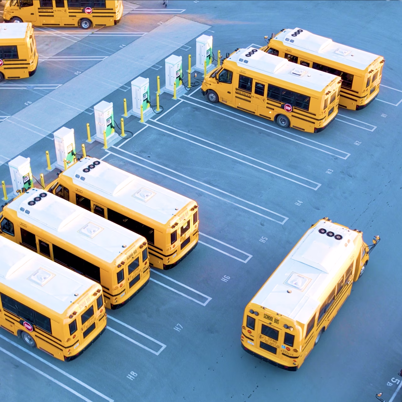 Aerial view of Zum Services, Inc. school buses parked in a marked lot alongside a row of EV charging stations.