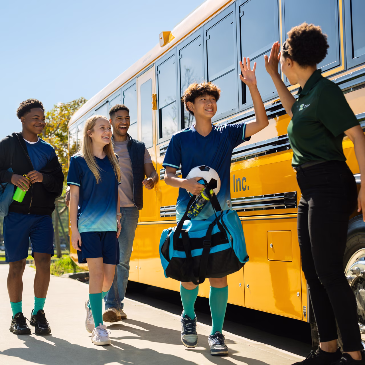 Students in soccer uniforms high-fiving a Zum Services, Inc. staff member beside a school bus after a field trip.