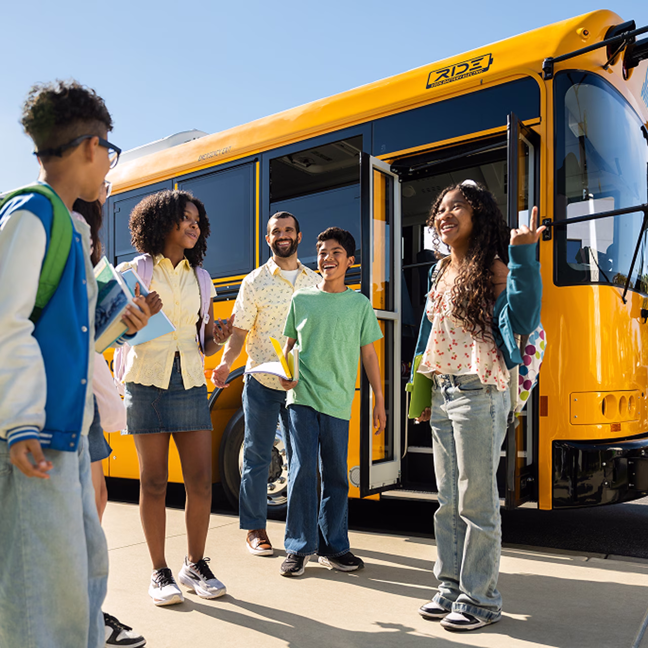 Students and a driver chatting and smiling in front of a Zum Services, Inc. school bus with its door open.