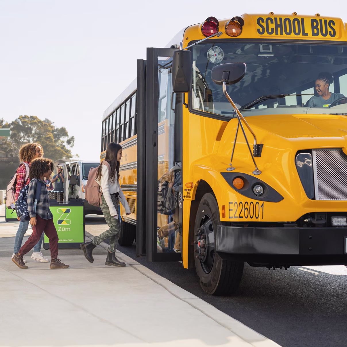 Students with backpacks boarding a Zum Services, Inc. school bus as a smiling driver waits at the wheel.