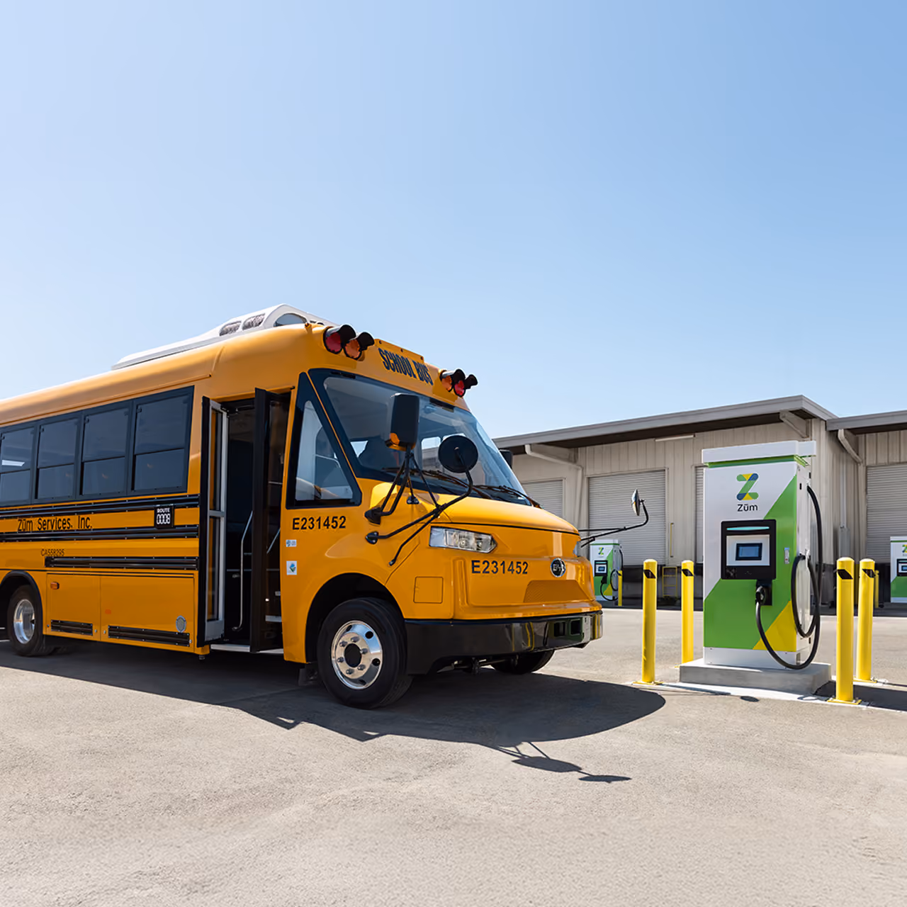 A Zum Services, Inc. school bus parked next to an EV charging station in a fleet yard.