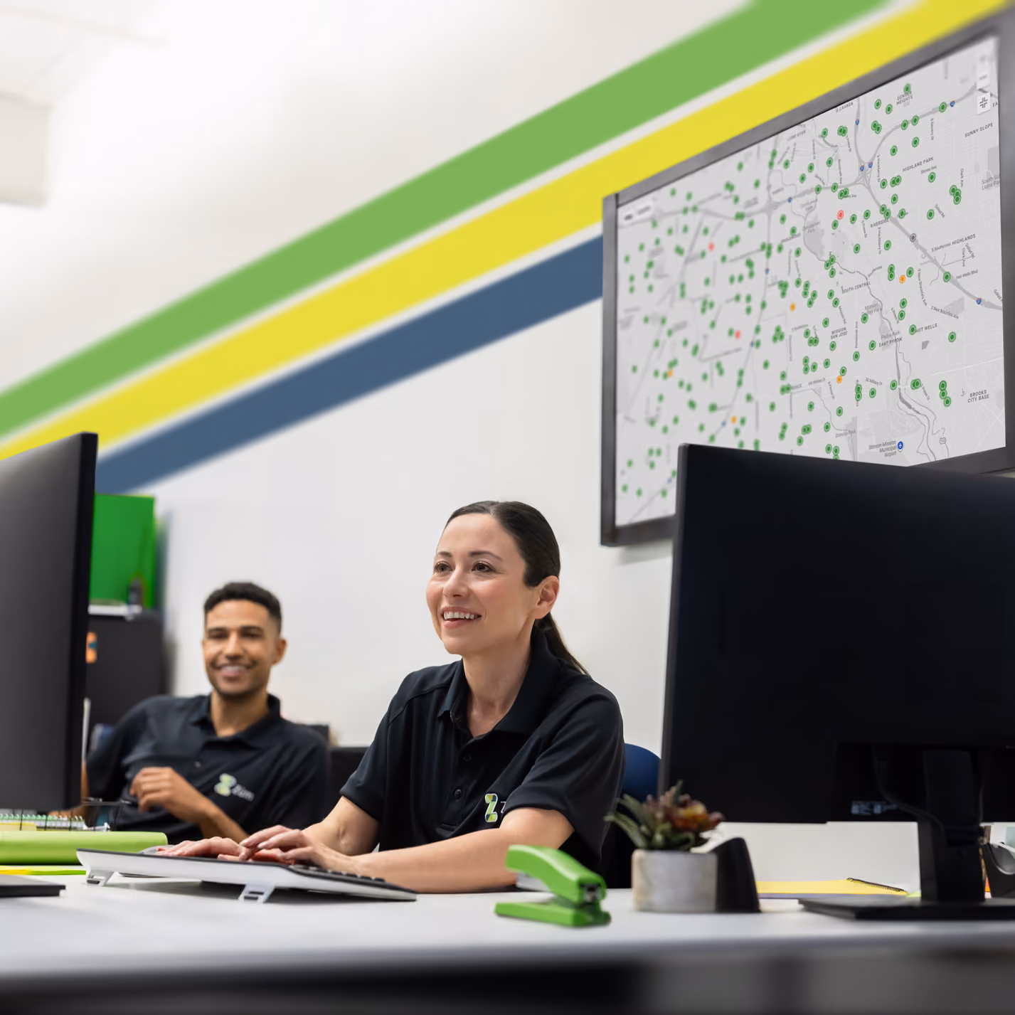 Zum Services, Inc. employees working at a dispatch center desk, with a live fleet tracking map displayed on a wall monitor.
