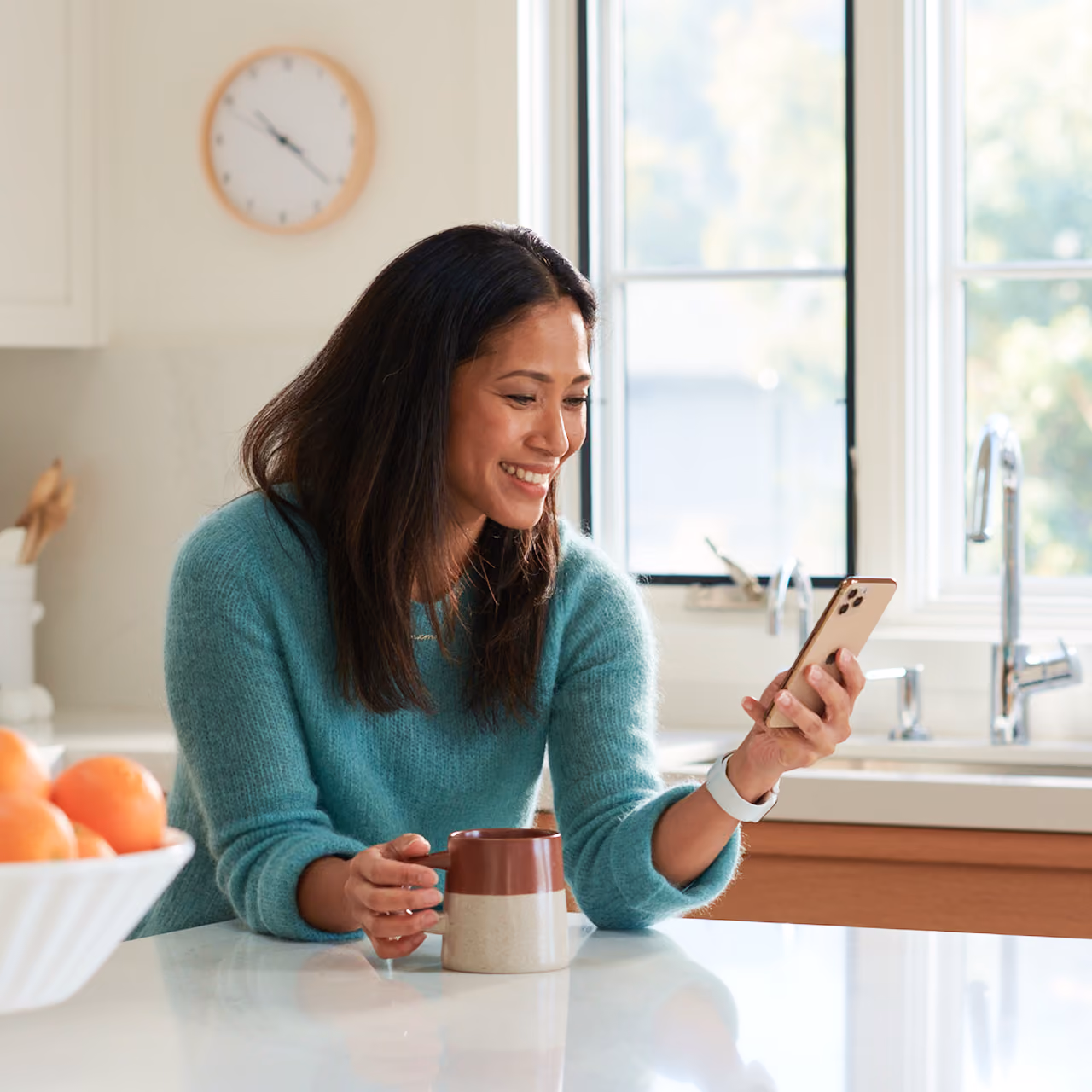 A parent smiling while checking Zum ride updates on her phone with coffee in hand at her kitchen counter.