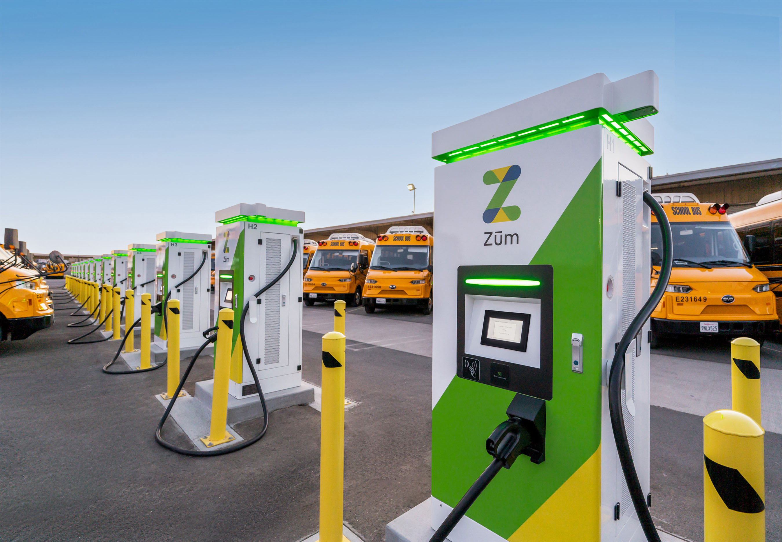 Electric vehicle charging stations lined up in a bus yard with school buses in the background.