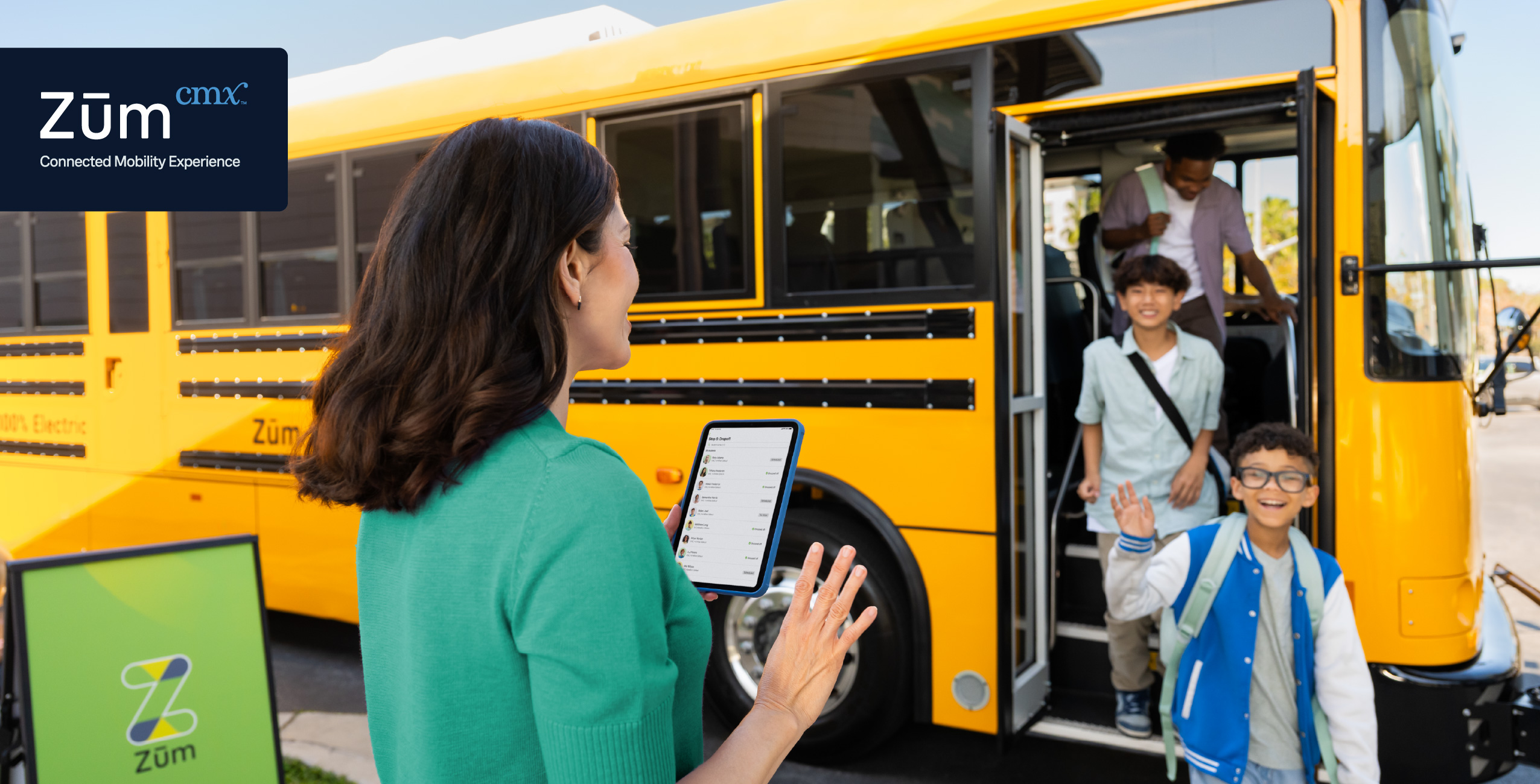 A woman with a tablet oversees students boarding a yellow school bus, smiling and waving.
