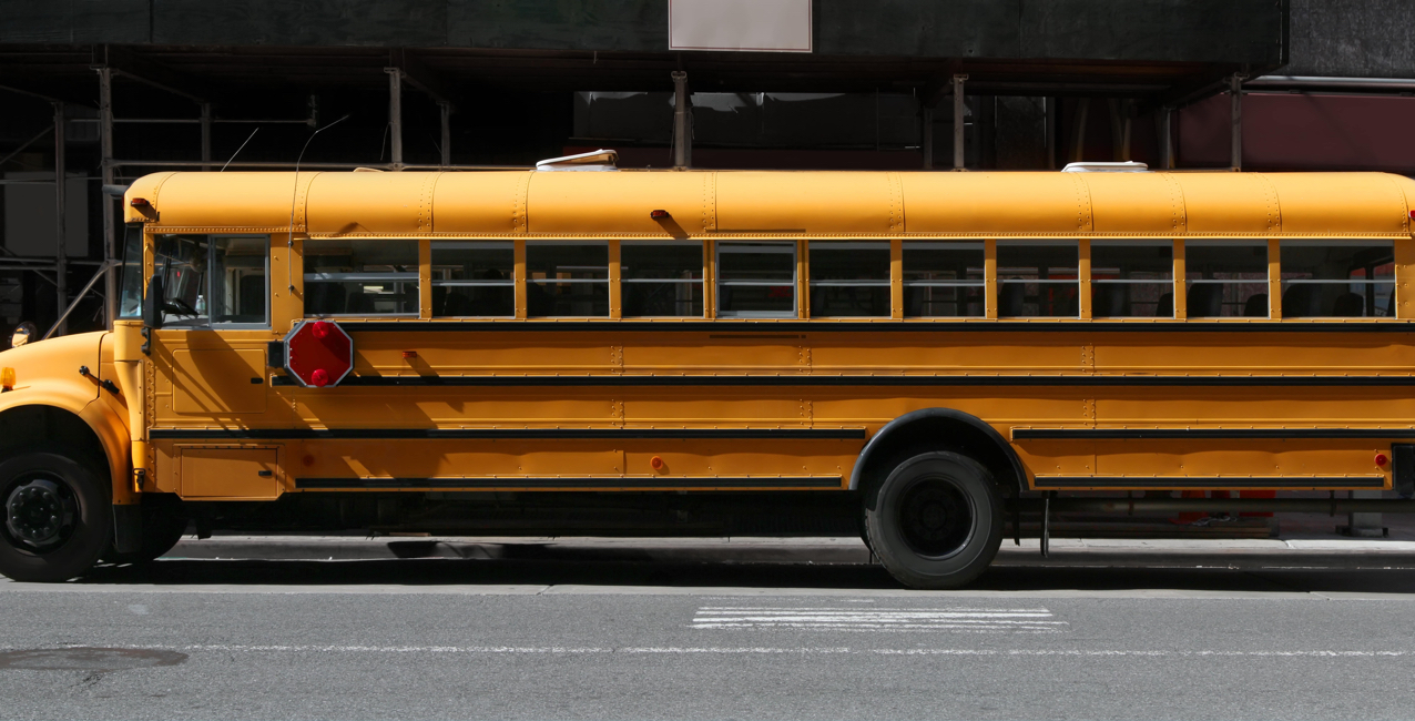 Yellow school bus parked alongside the street, showcasing its side view and large windows.