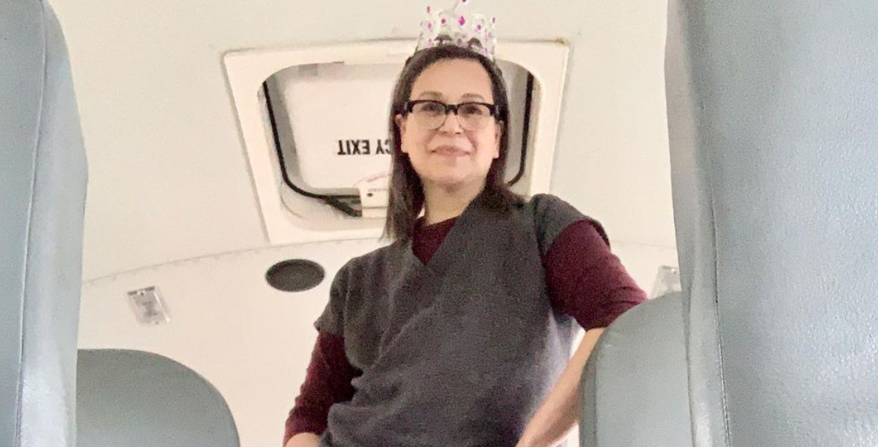 A woman with glasses and a tiara sits inside a bus, smiling at the camera.