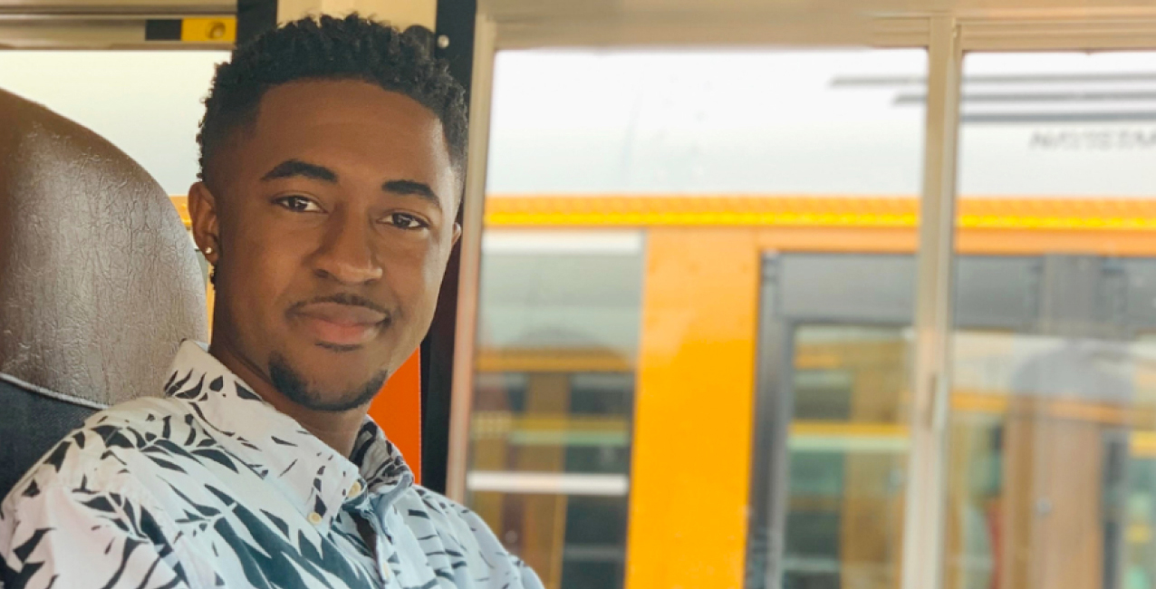 A young man smiles while sitting in the driver's seat of a school bus, ready to drive.