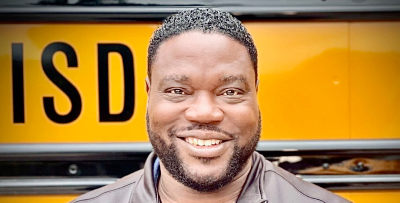 Curtis Jenkins smiles in front of a yellow school bus with "ISD" visible.