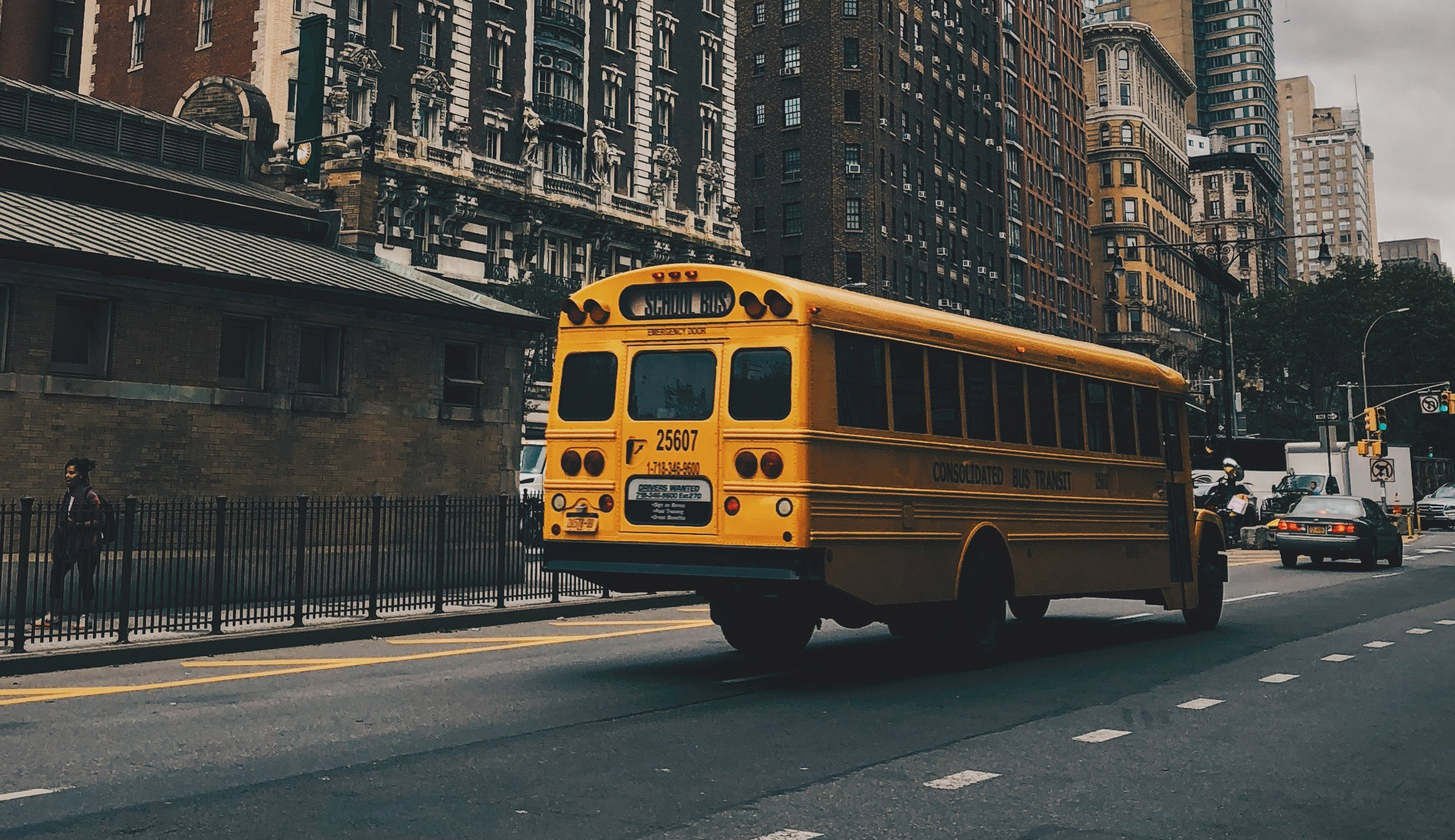 Yellow school bus driving down a city street with buildings in the background.