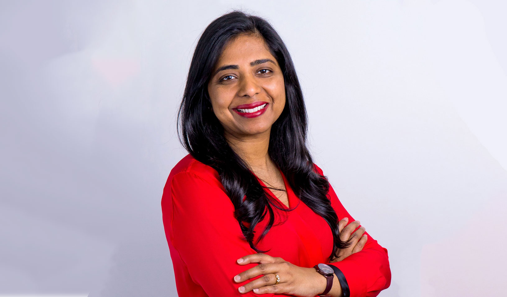Ritu Narayan, CEO of Zūm, smiles confidently with arms crossed in a red blouse.