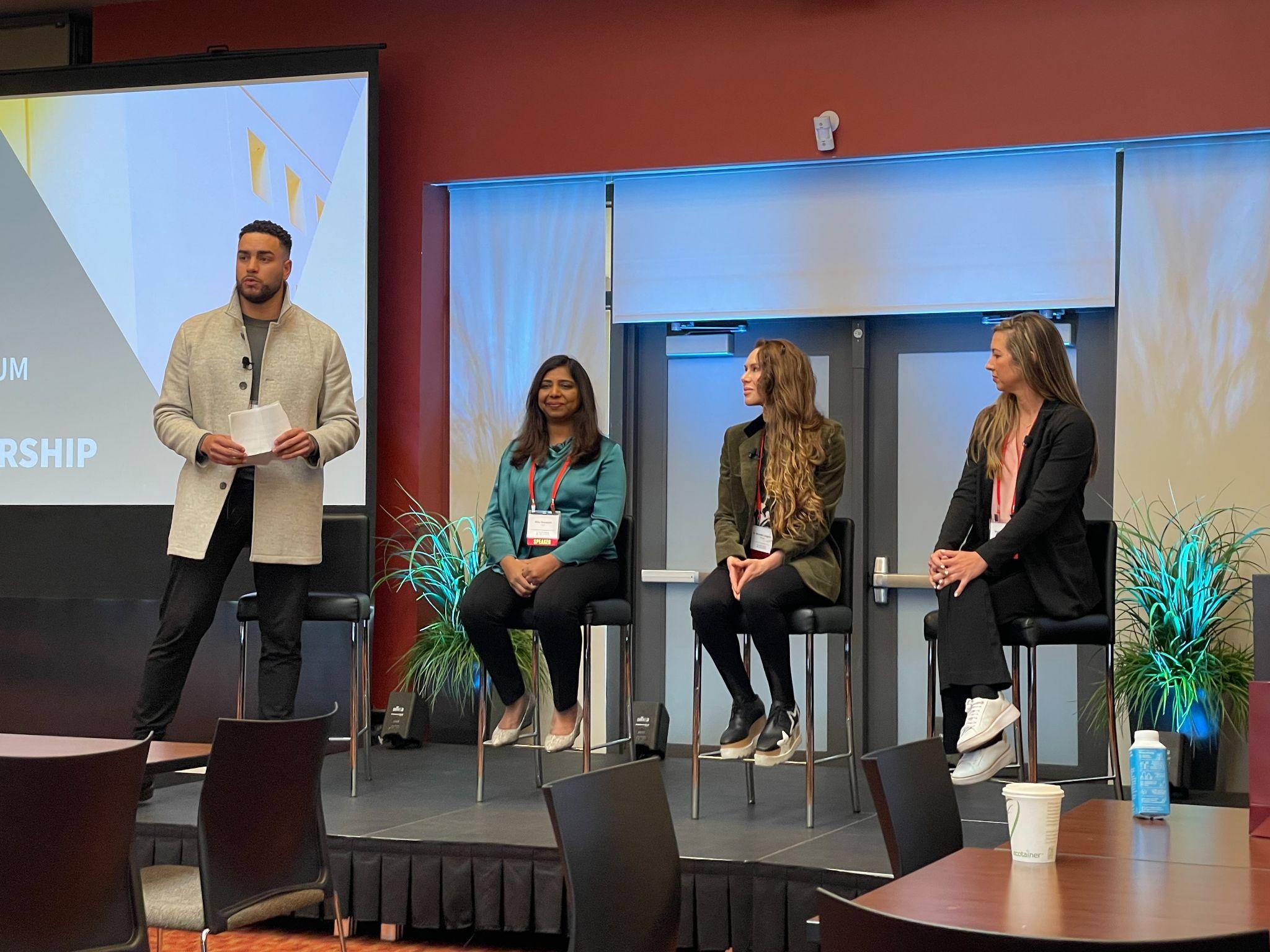 Panel discussion featuring four individuals on stage at a conference, discussing leadership topics.