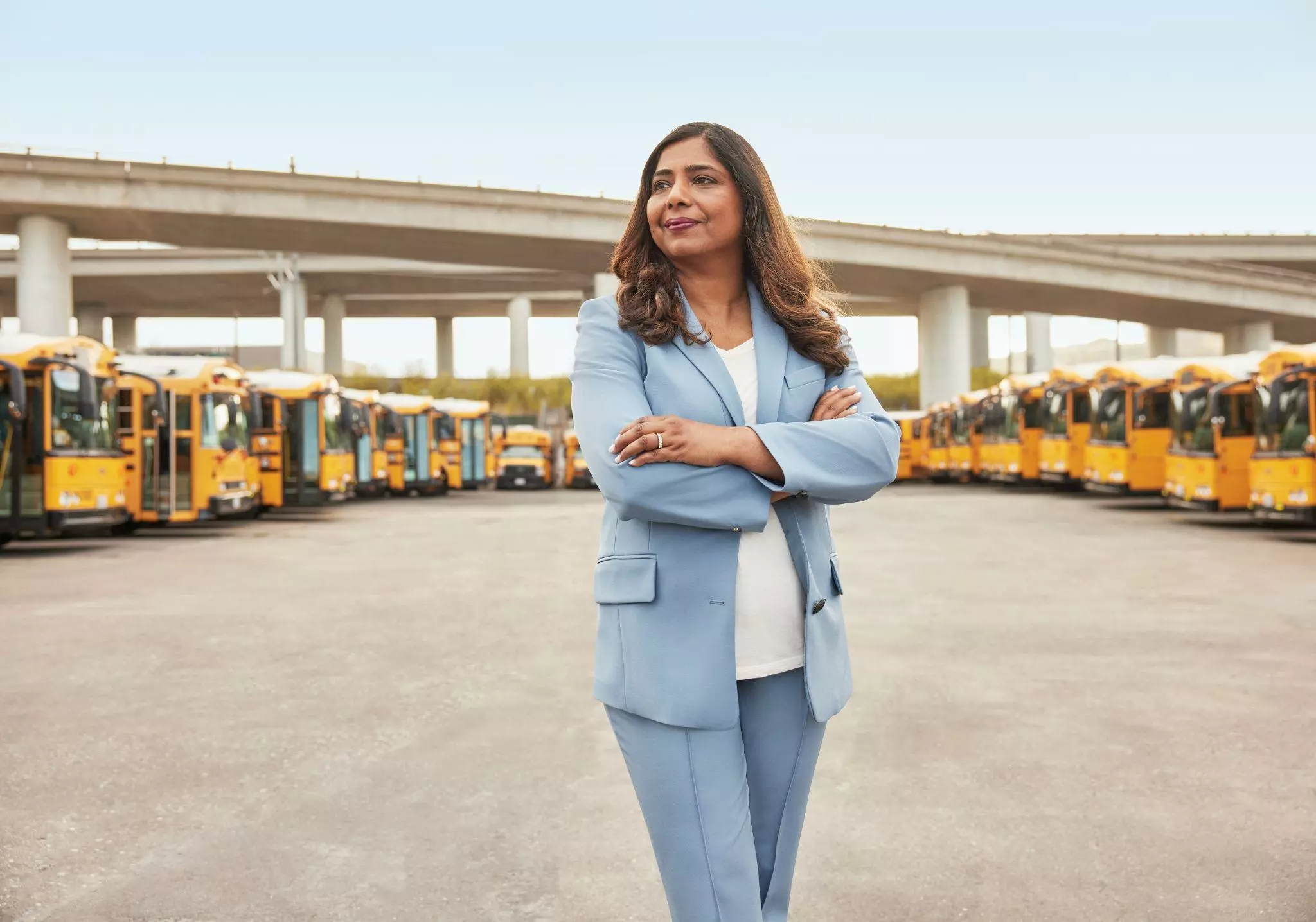 Ritu Narayan, Zum CEO, stands confidently in a bus yard with yellow school buses lined up.