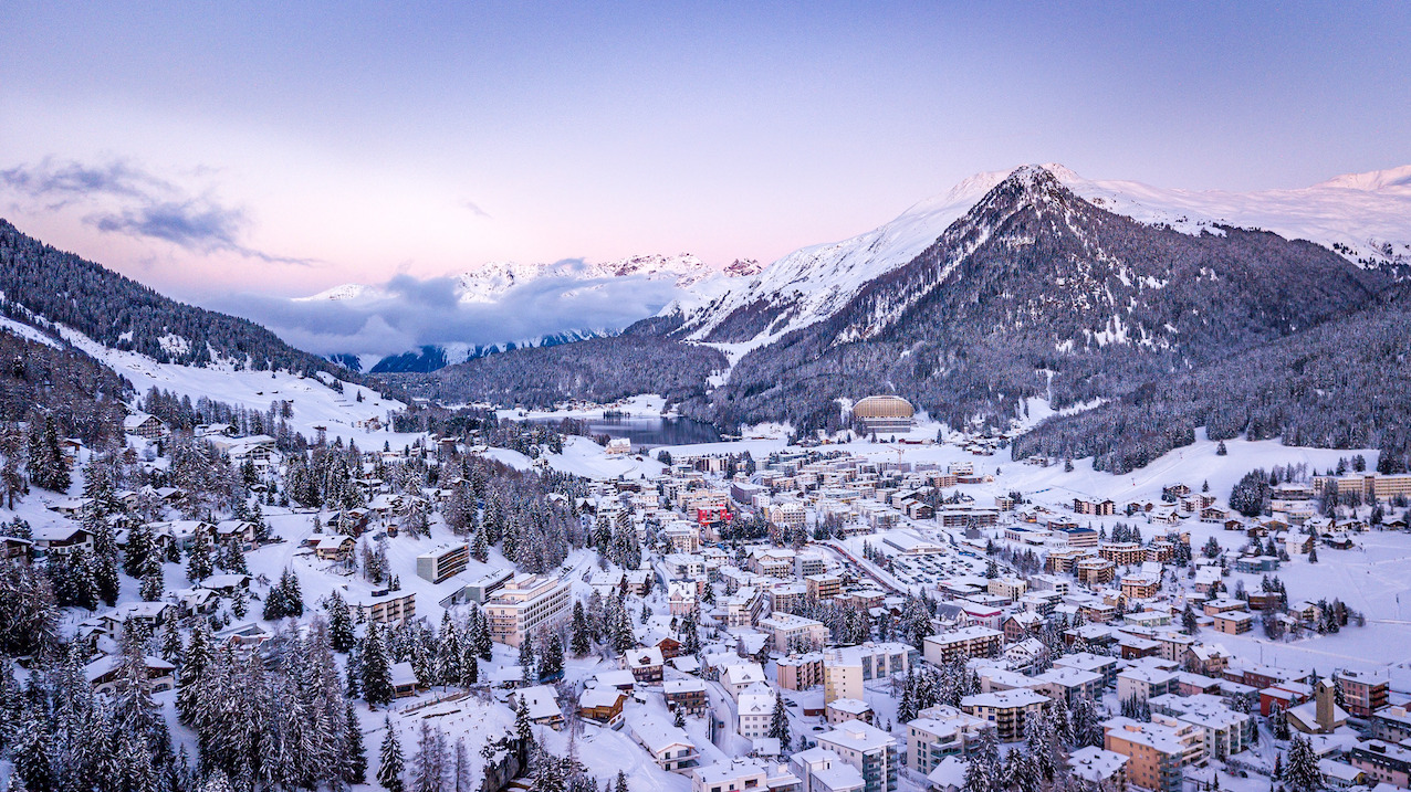 Snow-covered mountain town with buildings nestled among pine trees and alpine peaks in the