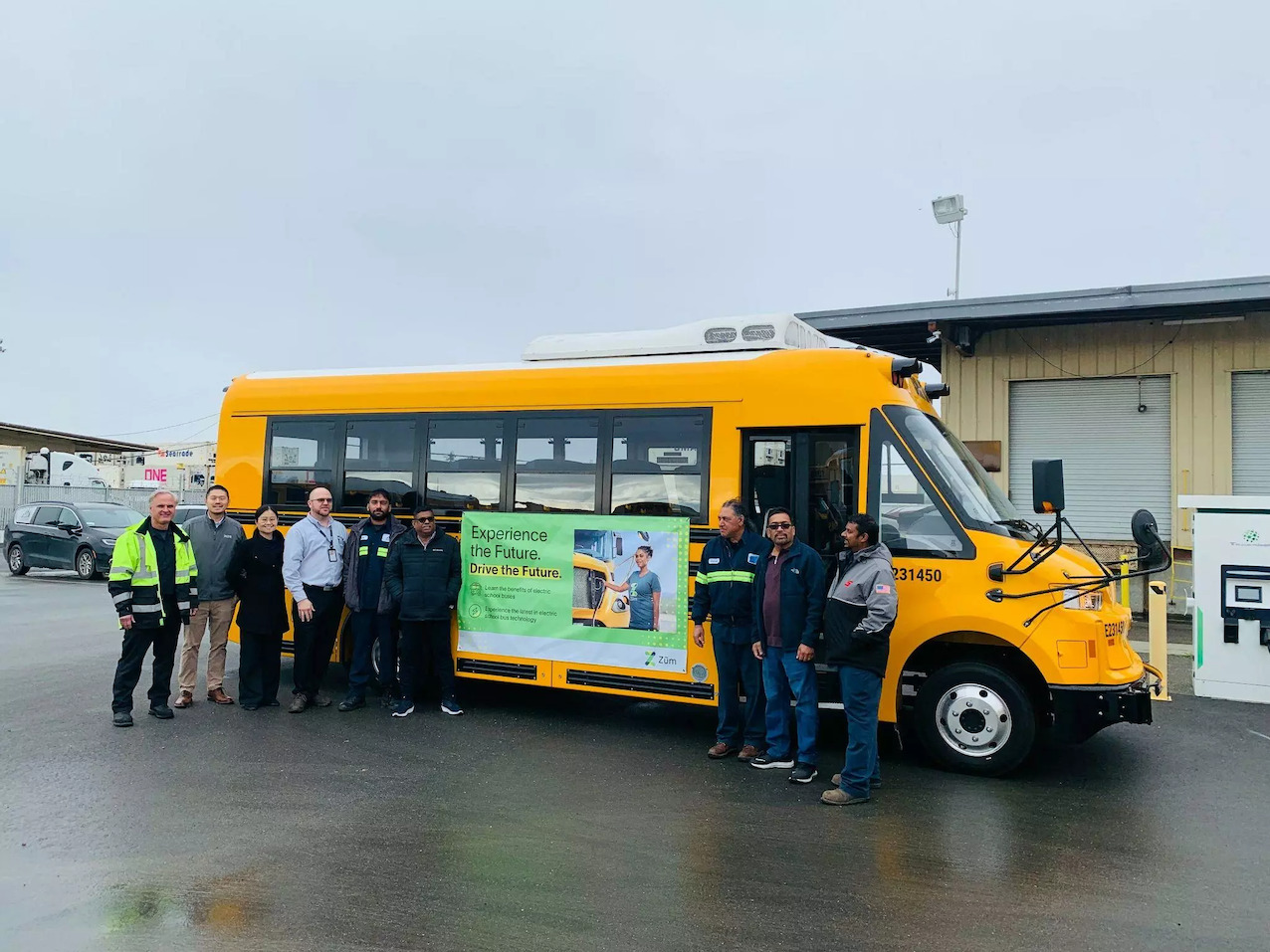 Group of Zum employees beside a yellow electric school bus with a promotional banner.
