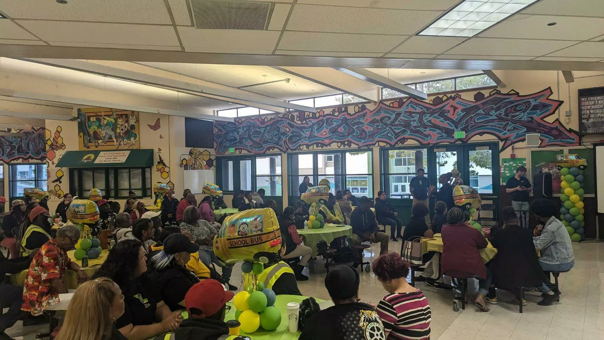 A group meeting with attendees seated at tables, discussing school transportation solutions.