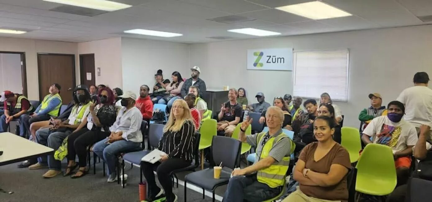 A group of drivers and staff seated in a training room for Zum. Brightly colored chairs are visible.