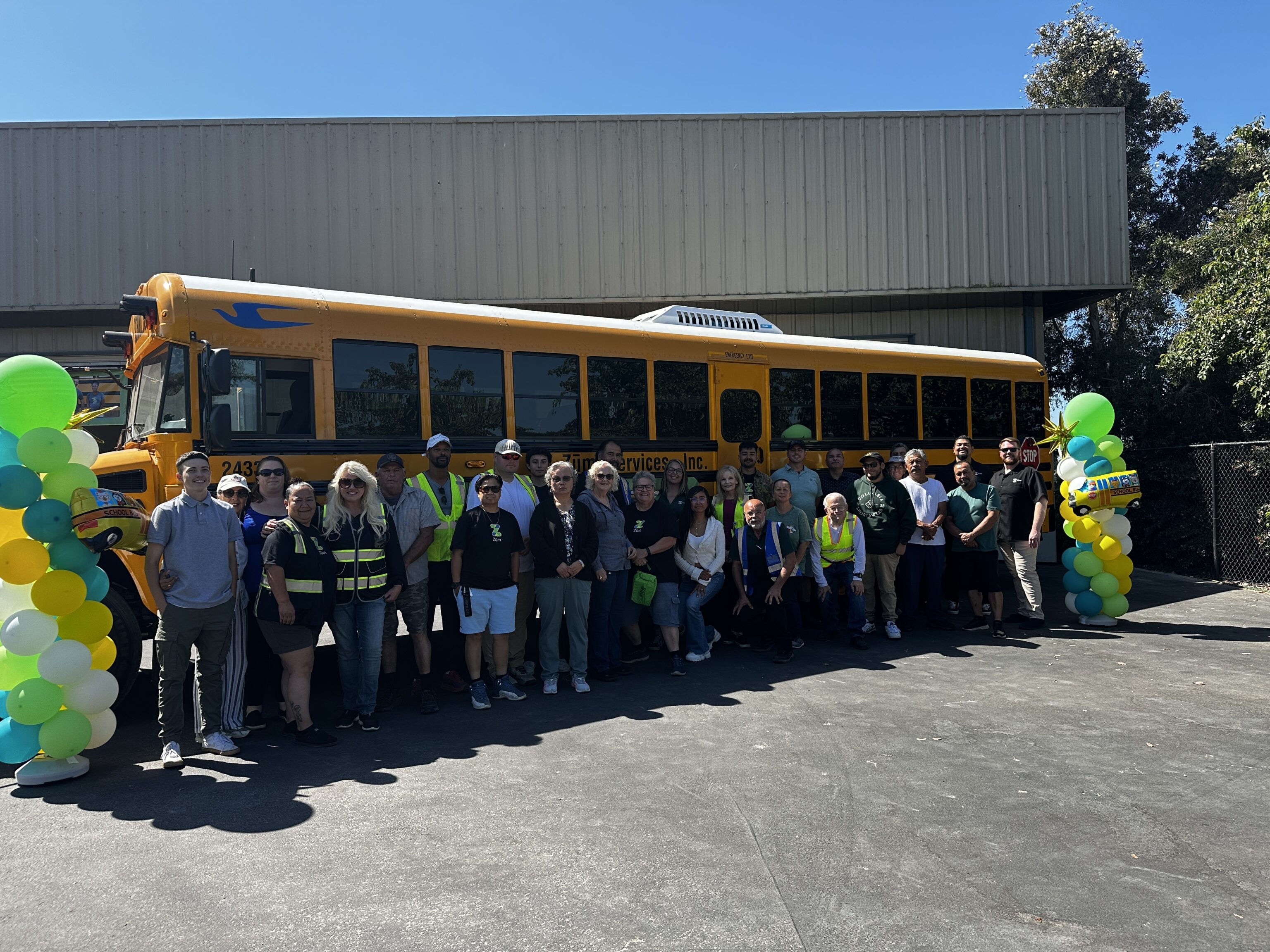 Group of Zum team members gathered in front of a yellow school bus with decorations.