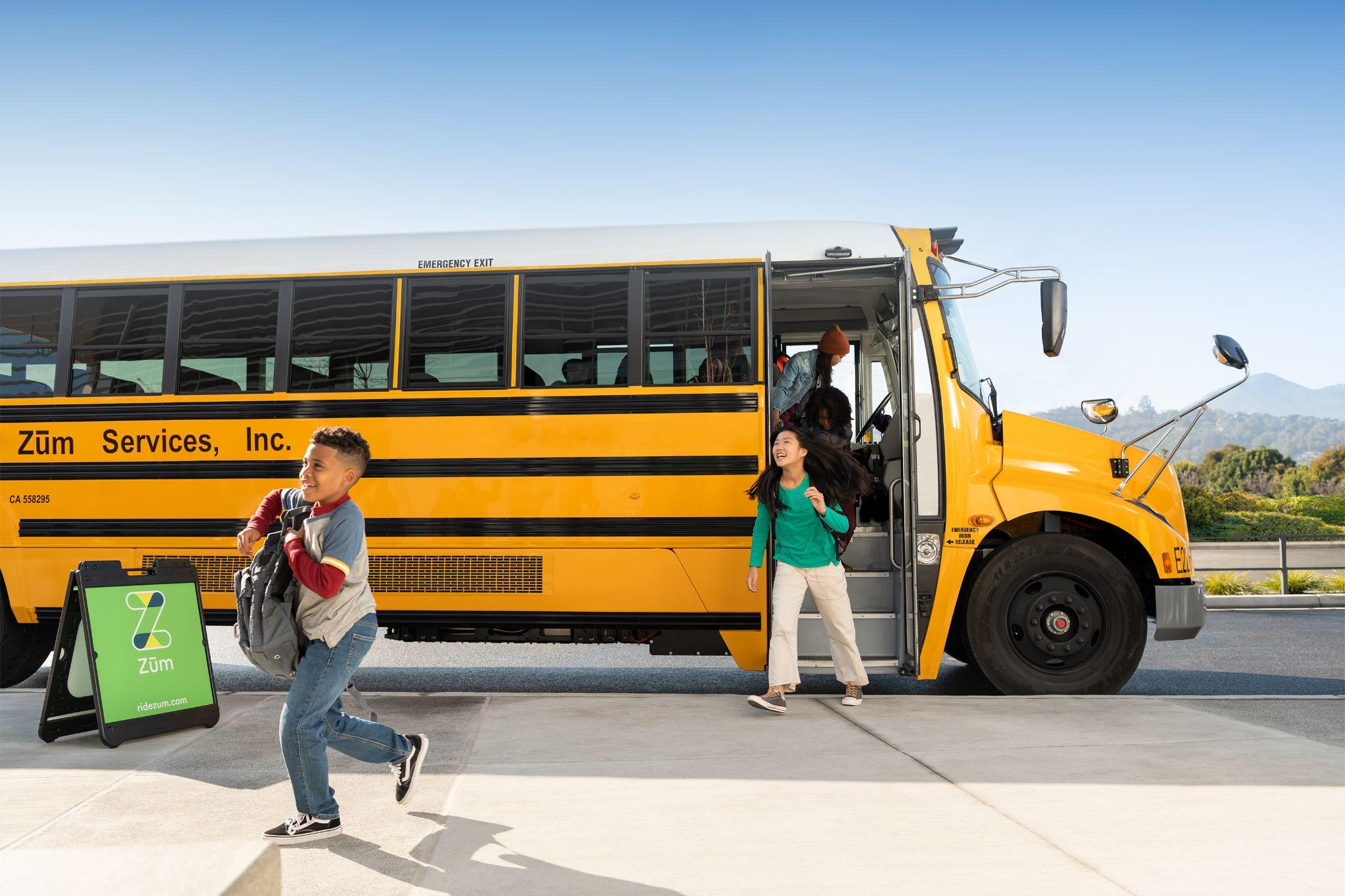 Students exiting a yellow school bus, with a Zum Services sign visible nearby.
