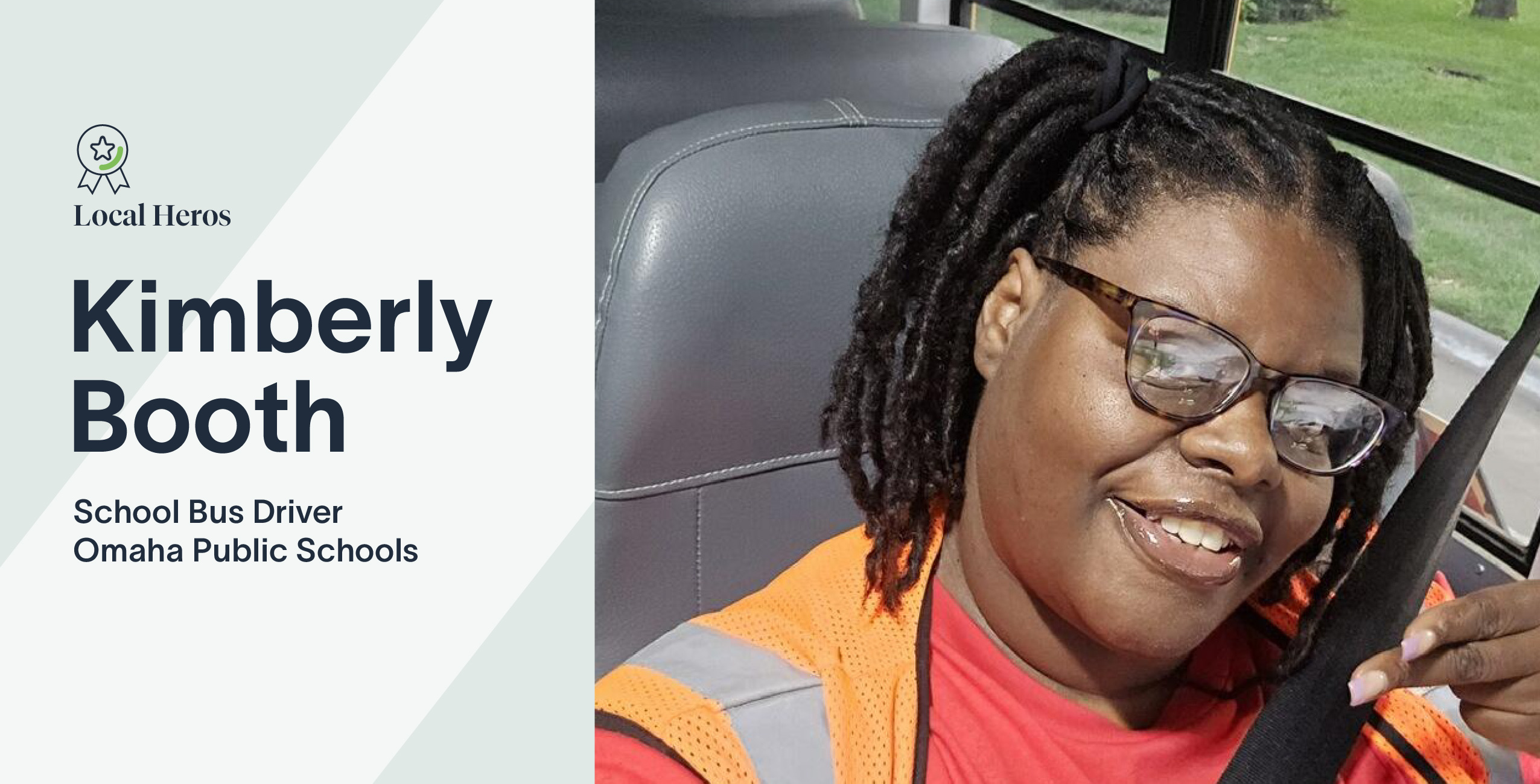 Kimberly Booth smiles while driving a school bus, wearing glasses and an orange safety vest.