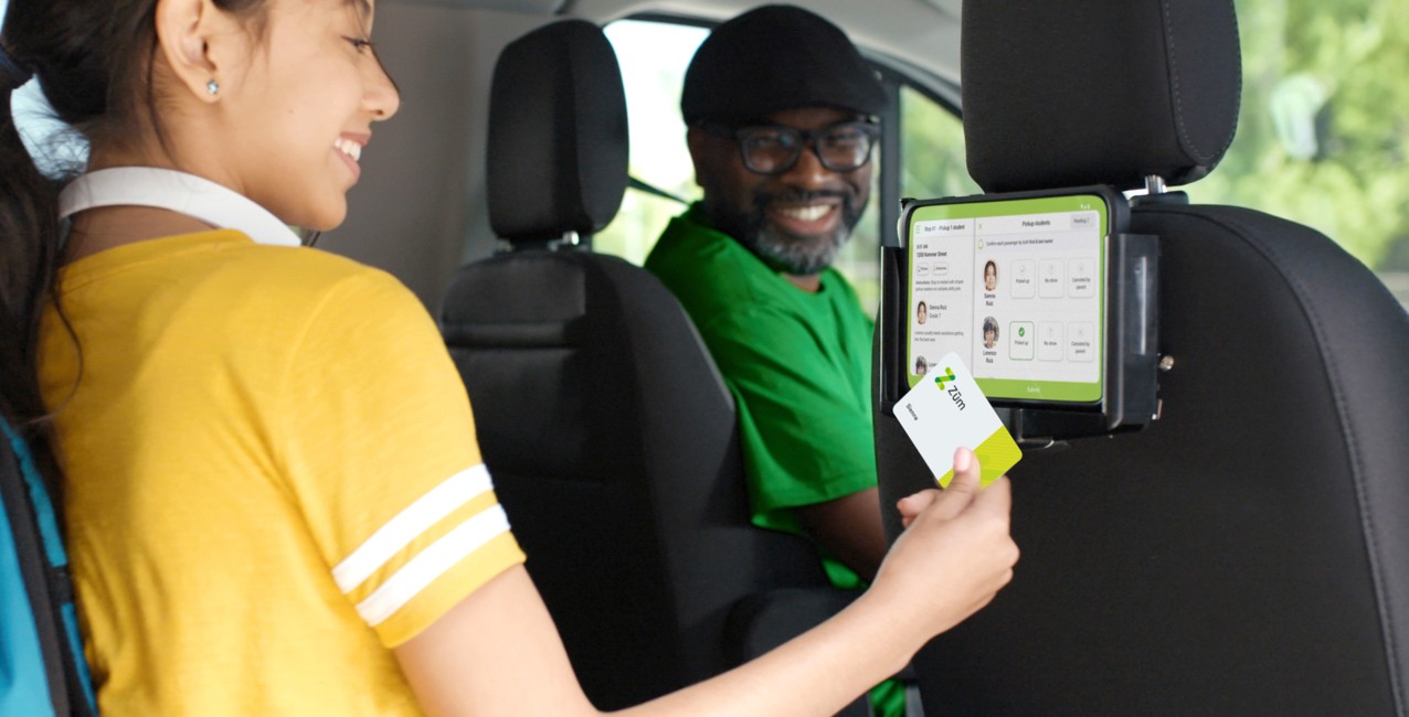 A girl using a transportation card and tablet inside a vehicle with a smiling driver.