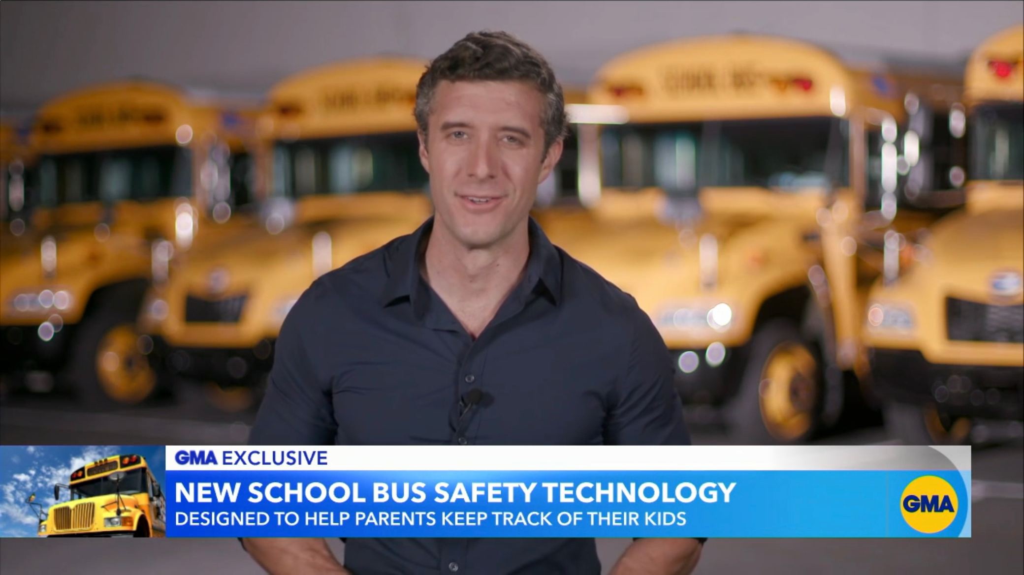 Male presenter discussing new school bus safety technology with yellow school buses in background.