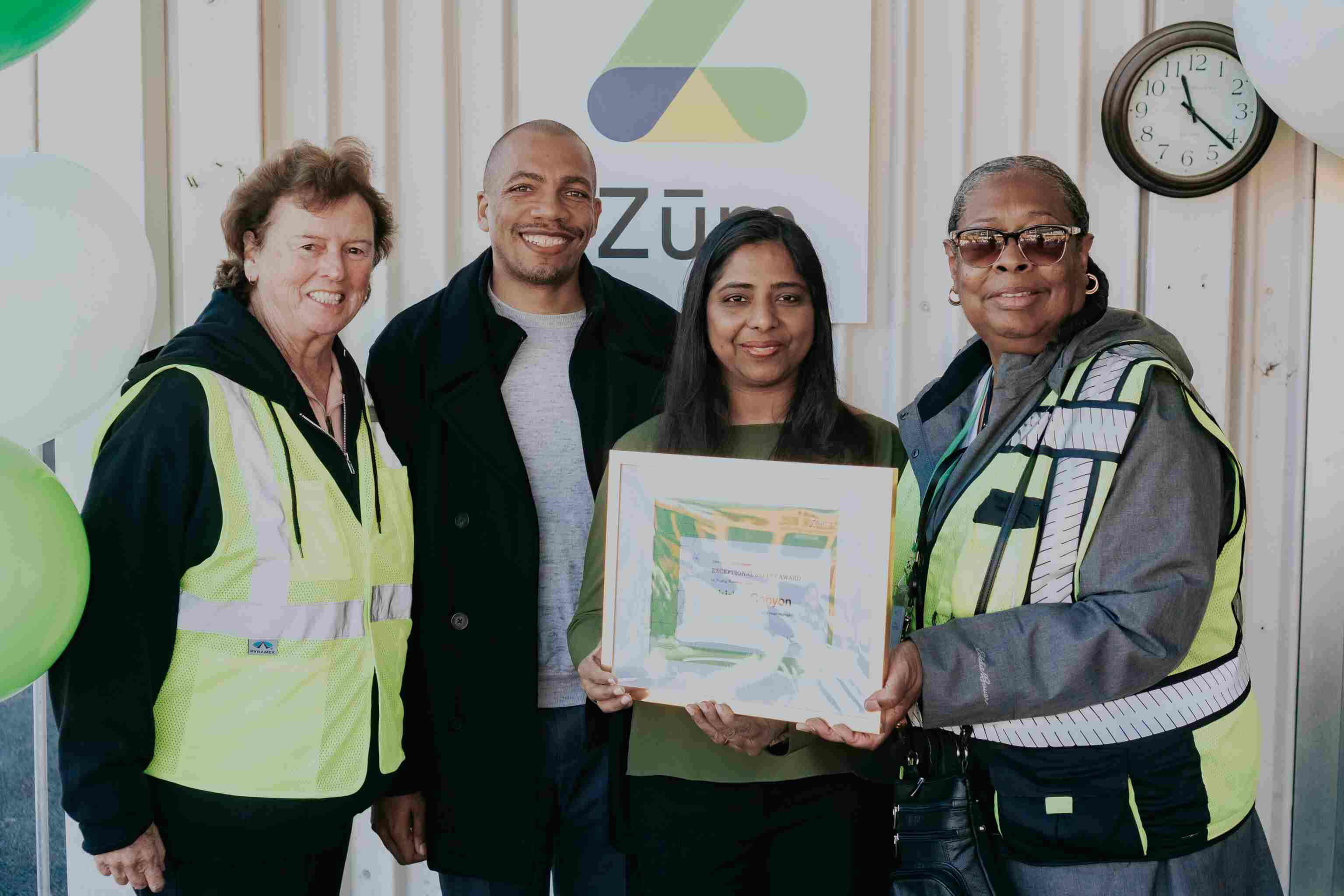 Group of four people, including Zum staff, holding a framed certificate in a school transportation