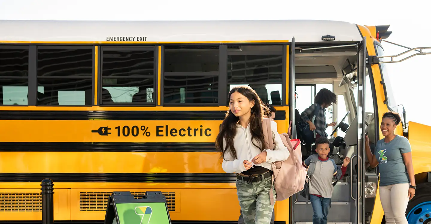 A student exits a yellow electric school bus while others disembark behind her.