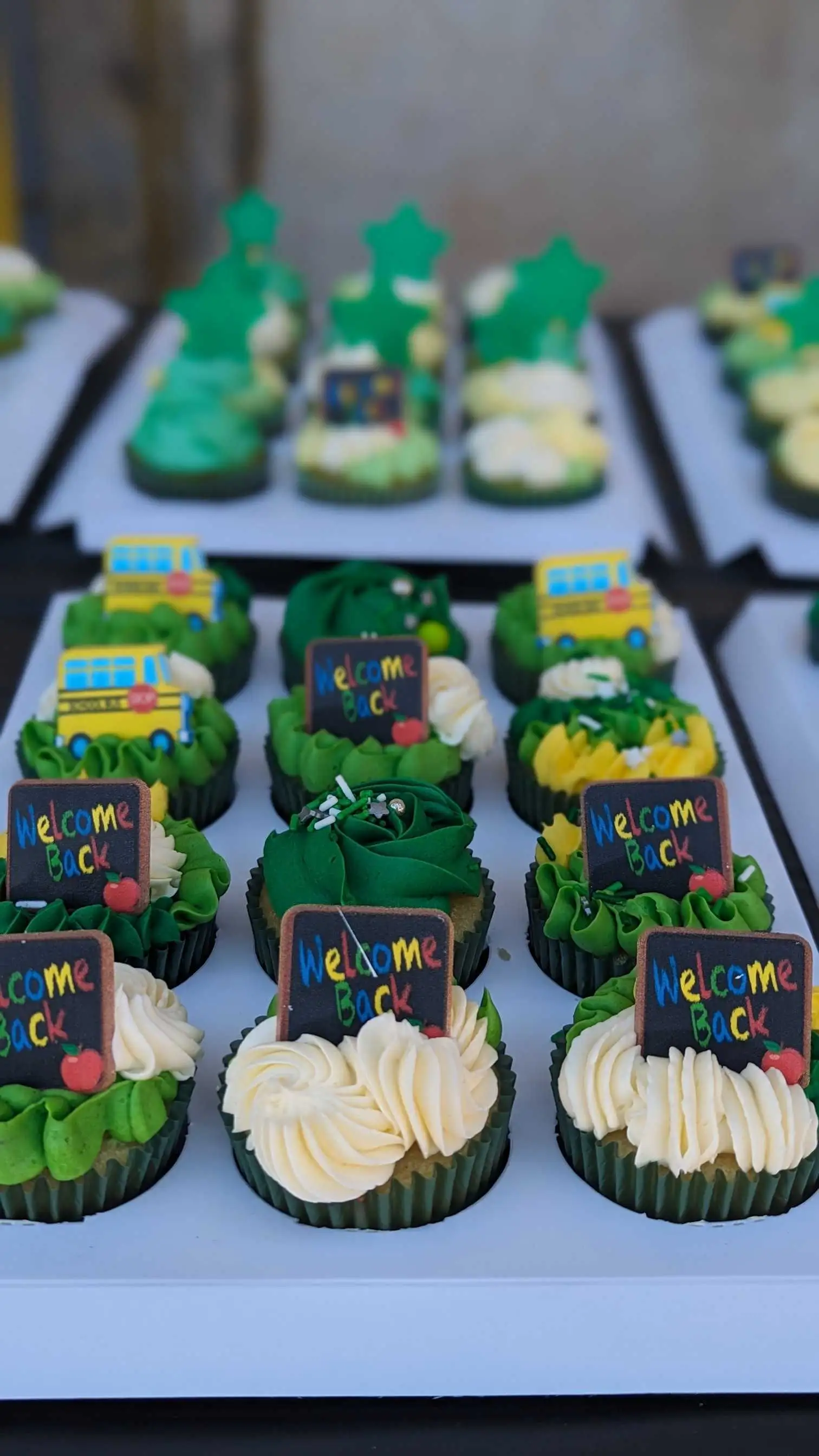 Colorful cupcakes decorated with "Welcome Back" signs, arranged on trays for a school event.