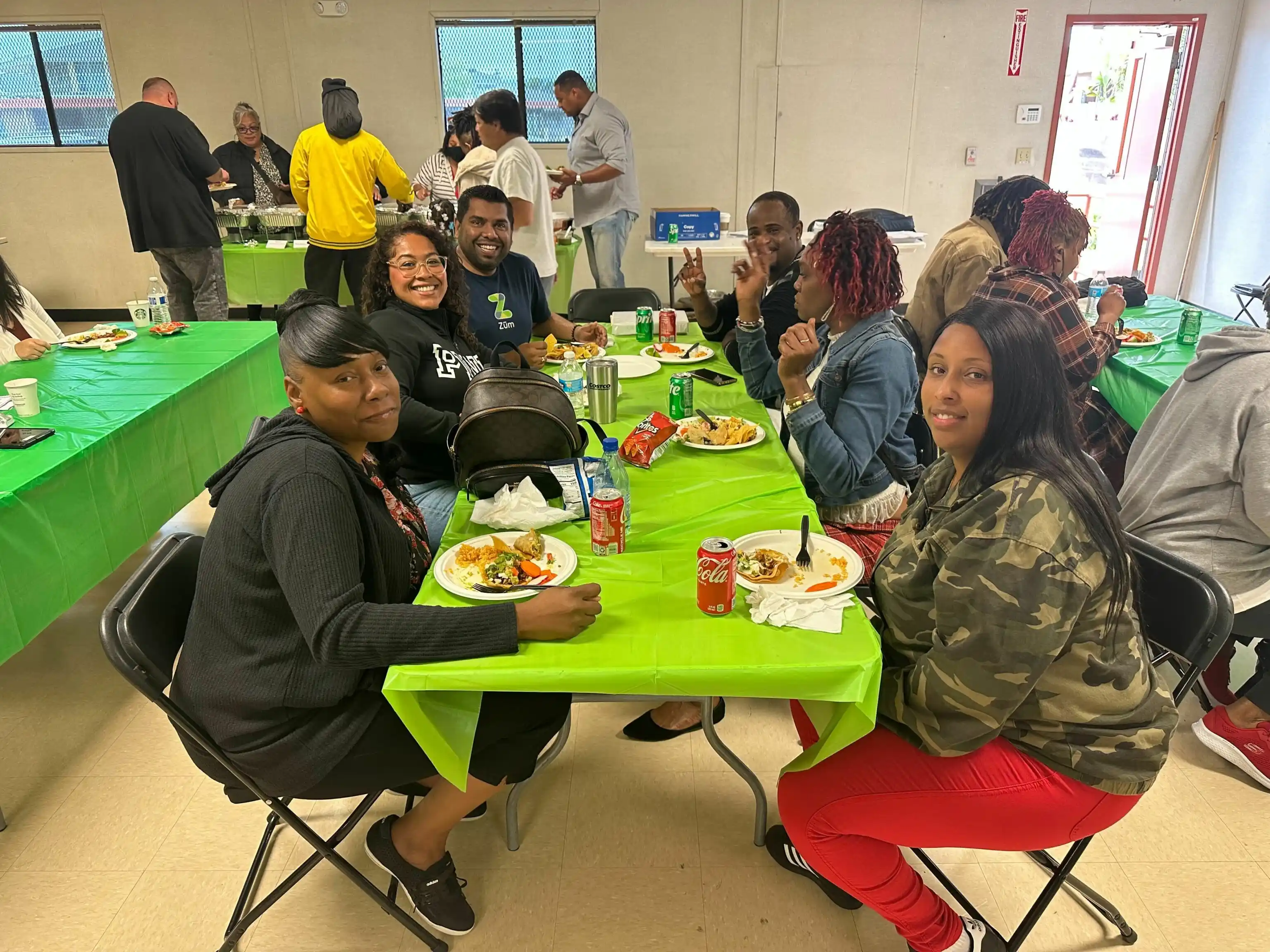 Groups of people enjoying a meal together at tables with green tablecloths in a community event.