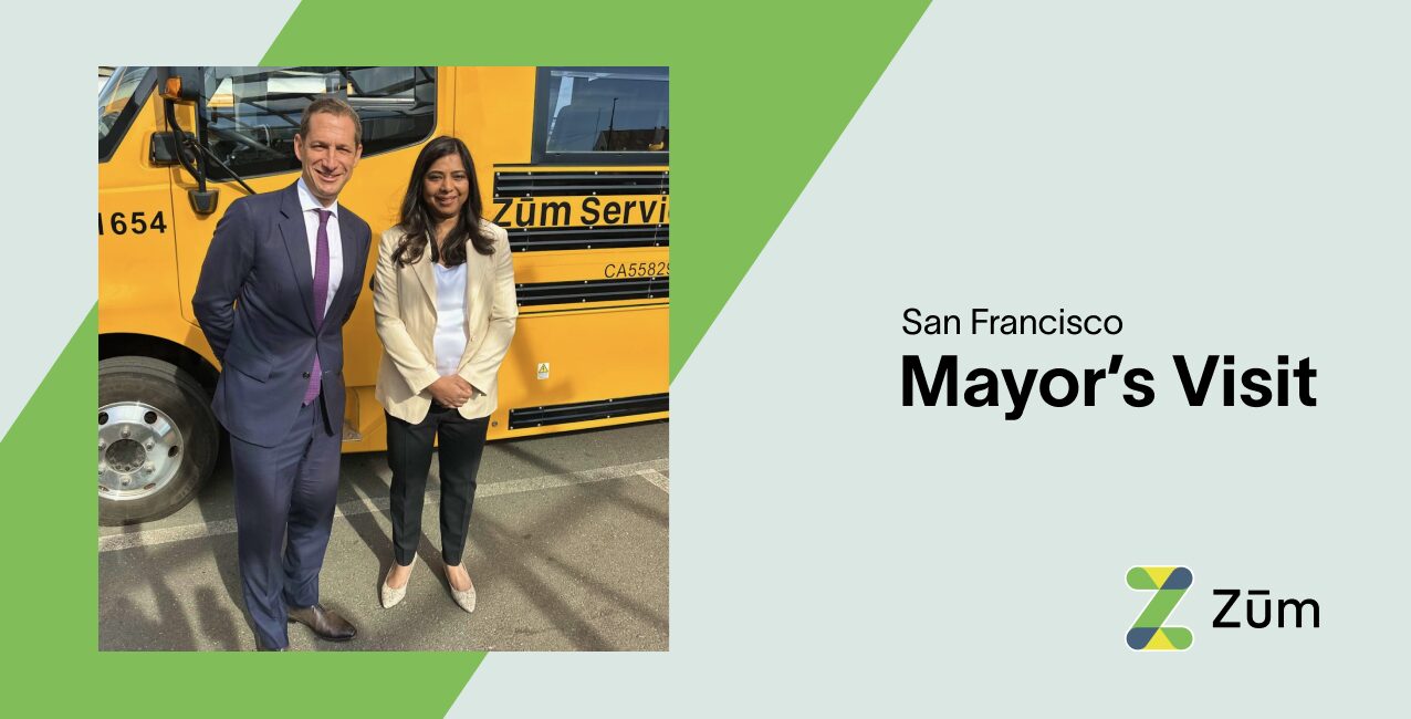 San Francisco Mayor Daniel Lurie poses with a Zum employee near a yellow Zum bus.