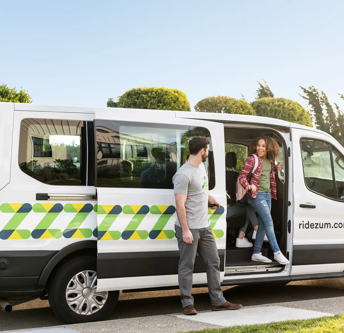 A driver assists a student exiting a Zum transportation van at a school pick-up location.