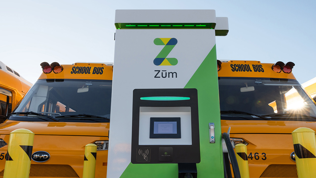 Zum electric school bus charging station with two yellow school buses in the background.