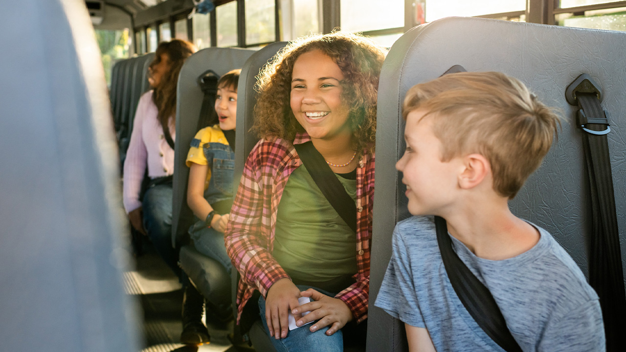 Students on a school bus smiling and chatting, showcasing a friendly transportation environment.