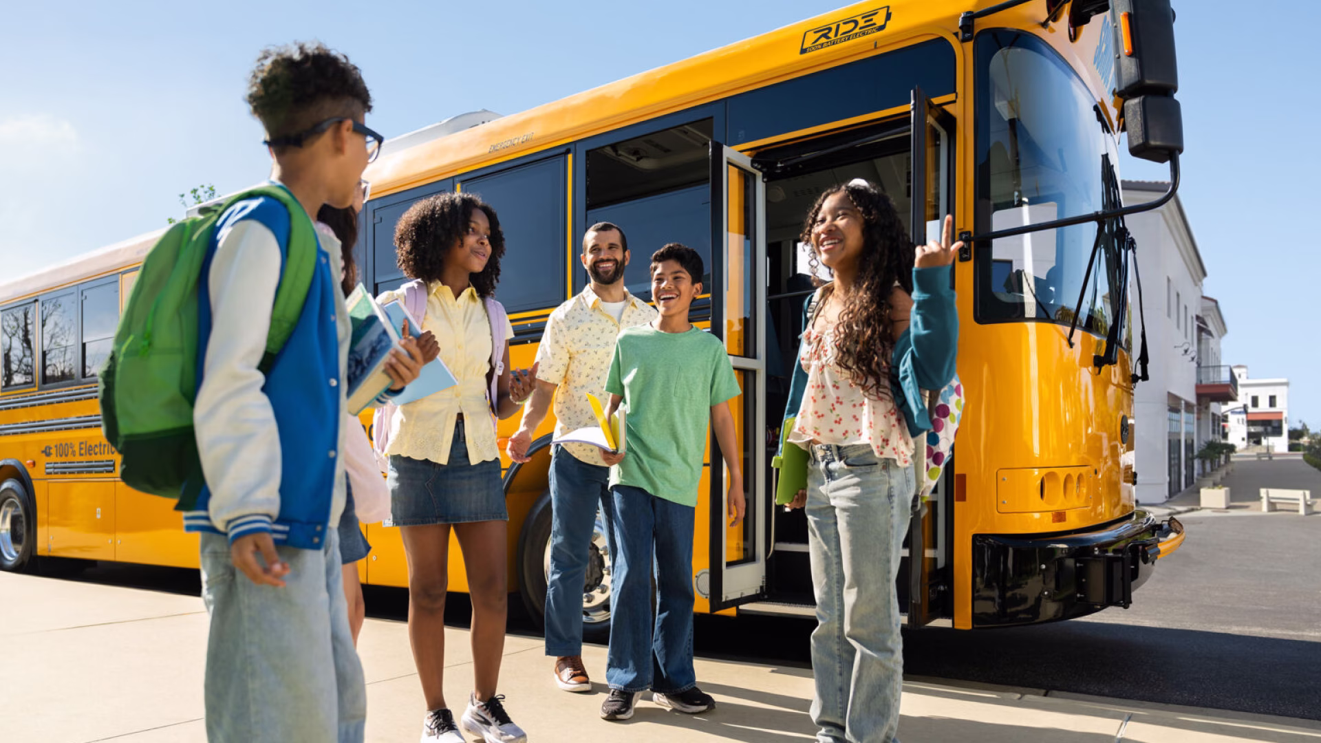 Students and adults smiling while boarding a yellow school bus with an open door.