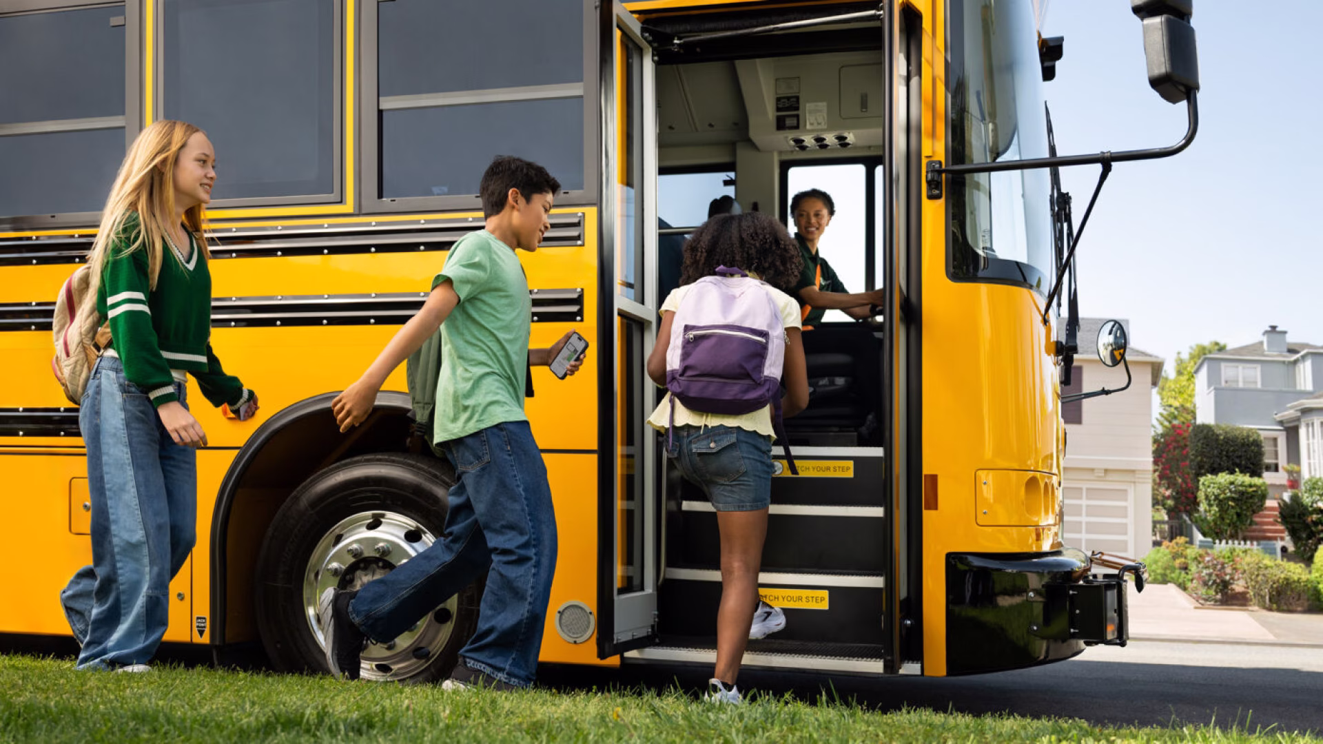 Students boarding a yellow school bus while a driver assists from the front.