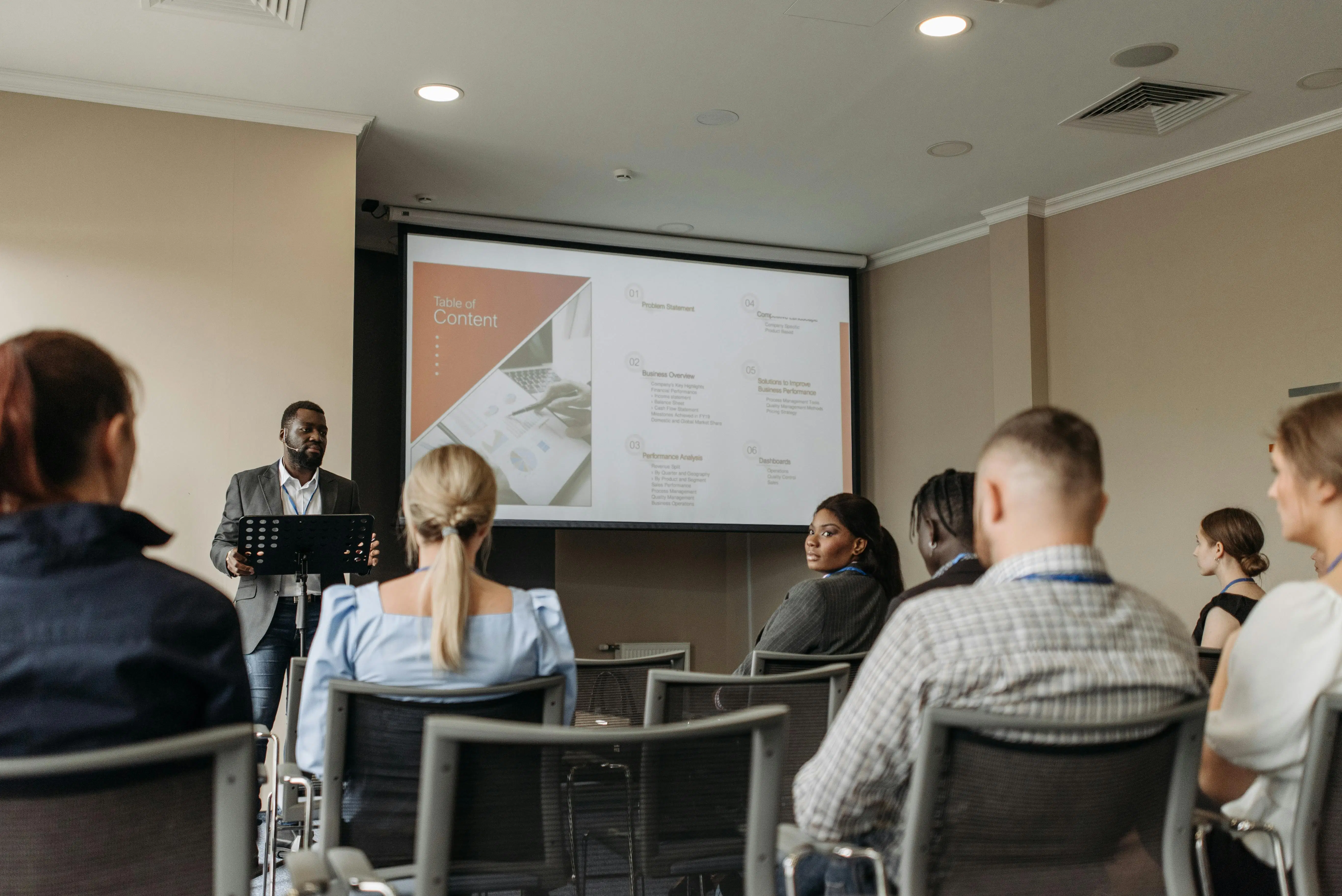 A consultant delivering a business performance presentation to a group of professionals in a conference room.