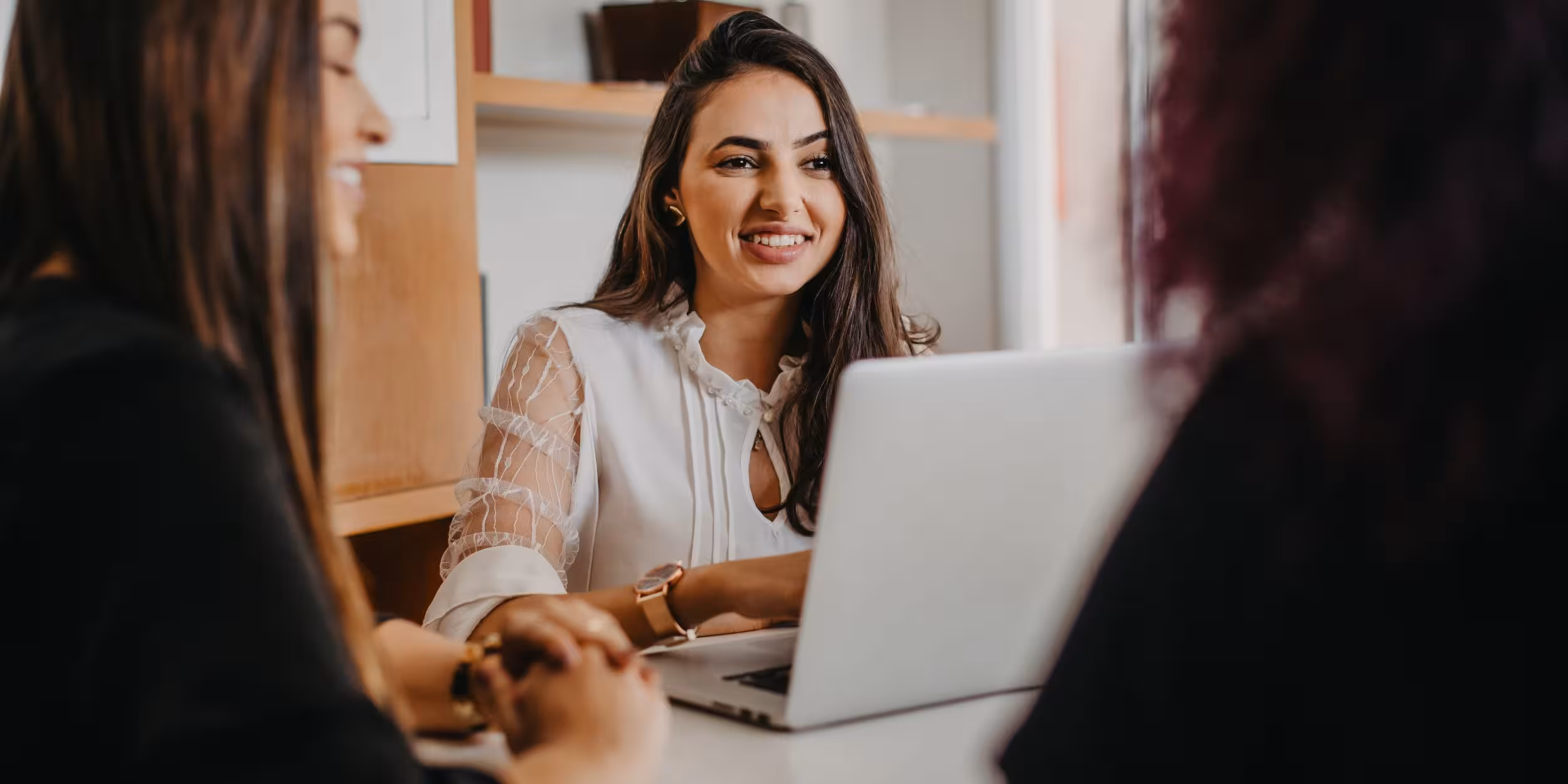 Woman smiling with laptop in front of her, talking to two people