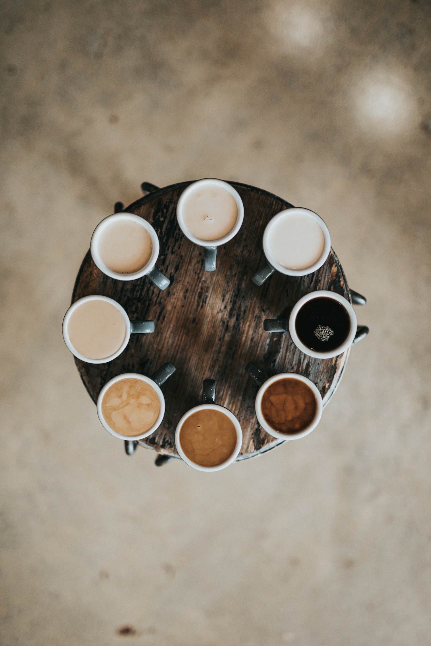 Overhead view of eight coffee cups arranged in circle on wooden tray