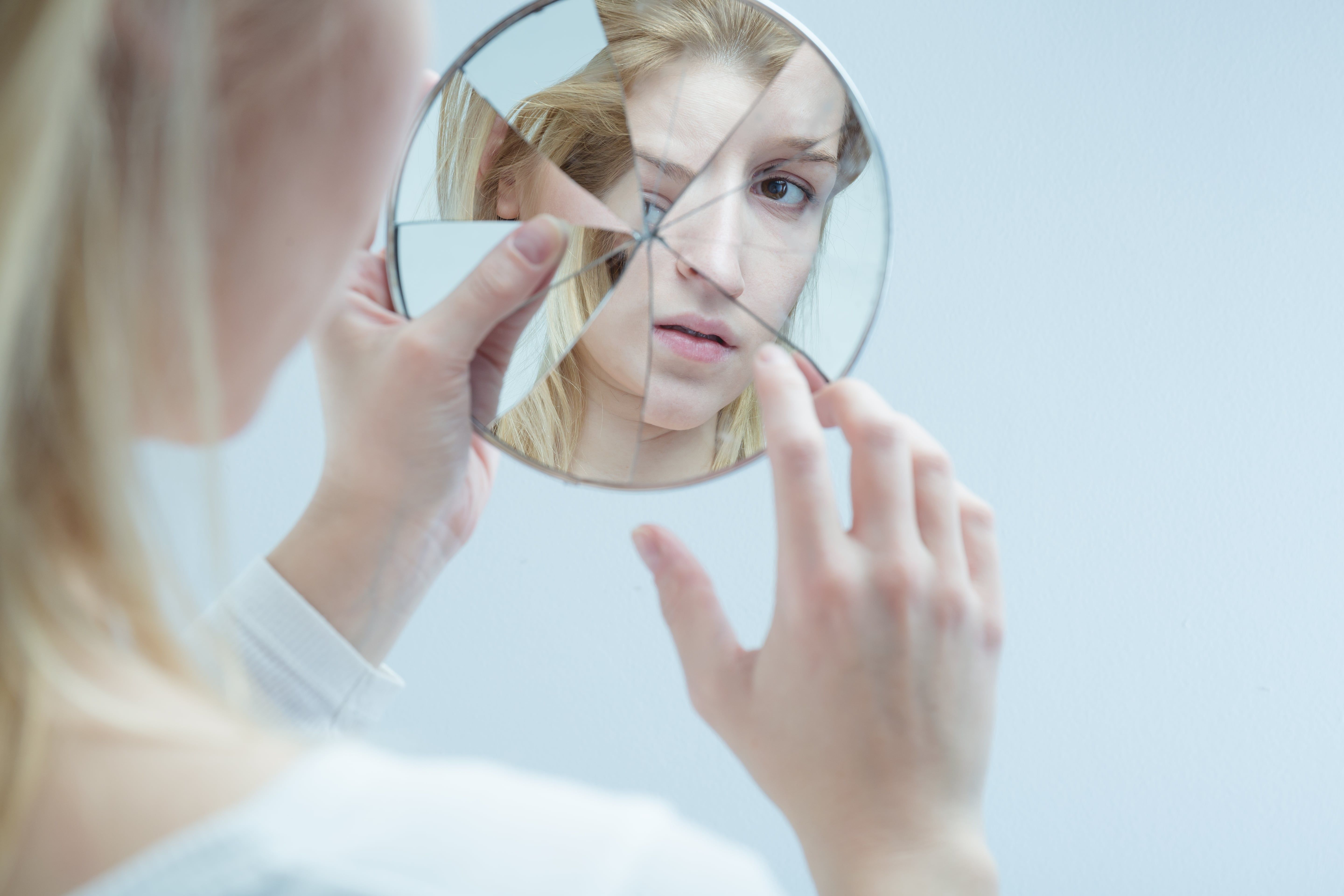 Woman holding broken mirror reflecting fragmented face image