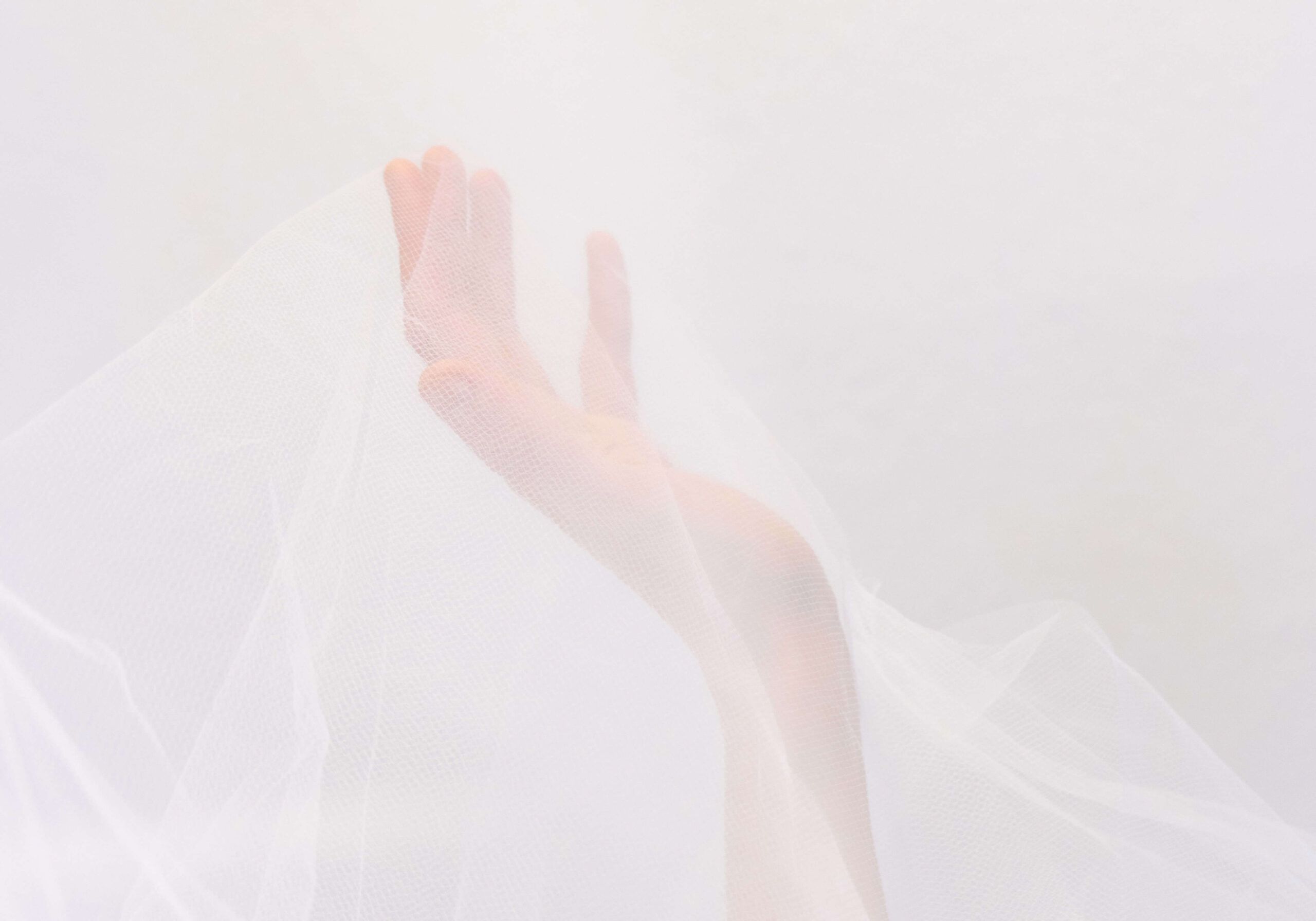 Soft, blurred image of an outstretched hand with gentle pink and white tones against neutral background