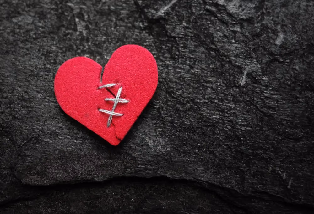 Red broken heart stitched with thread on dark textured background
