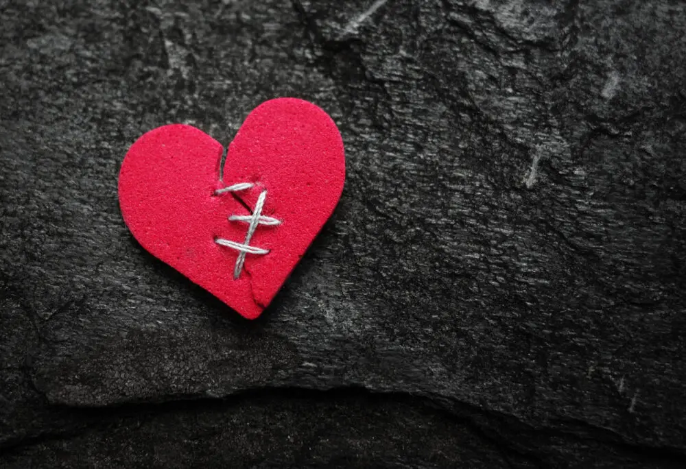 Red broken heart stitched with thread on dark textured background