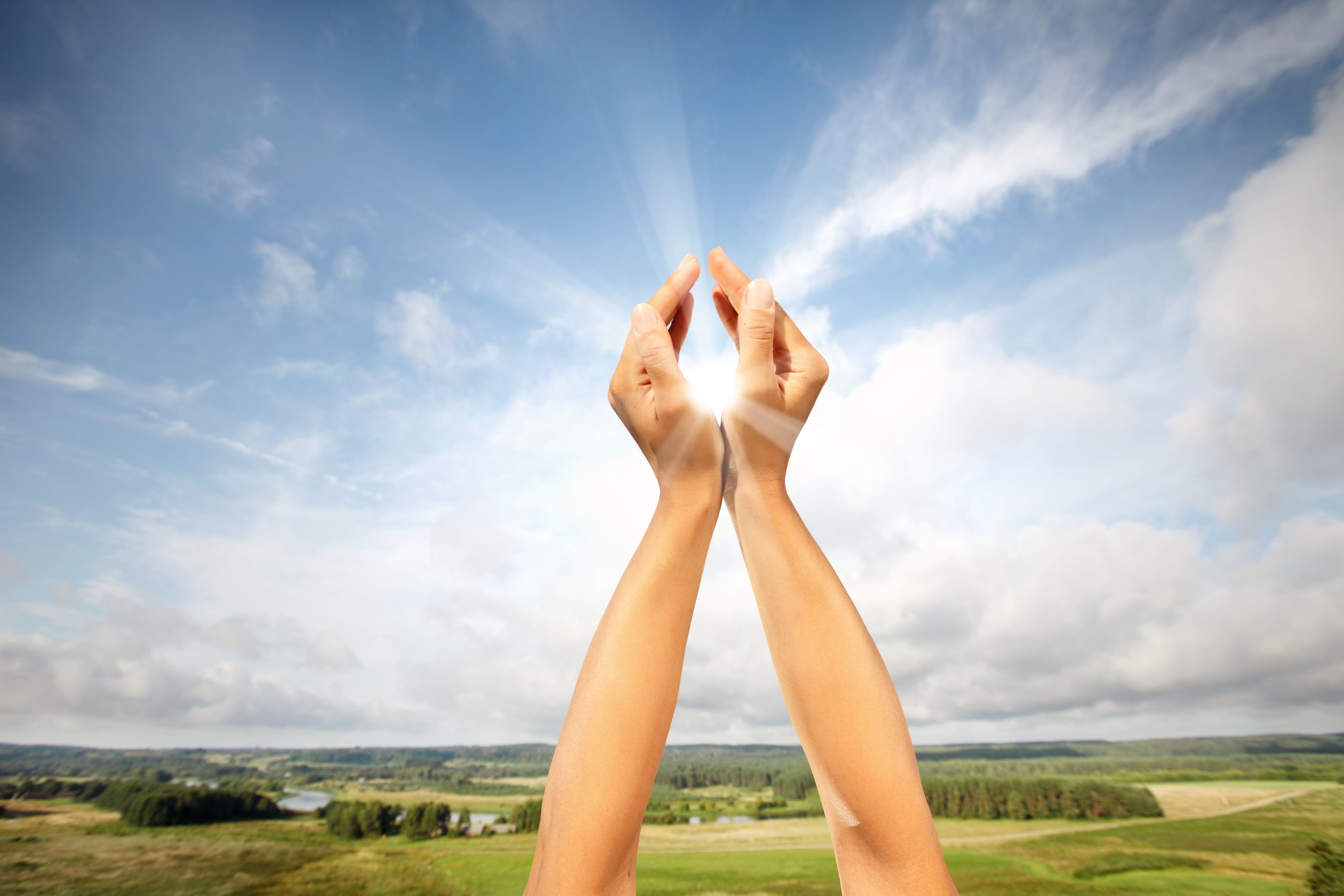 Hands forming heart shape around sun over scenic green landscape