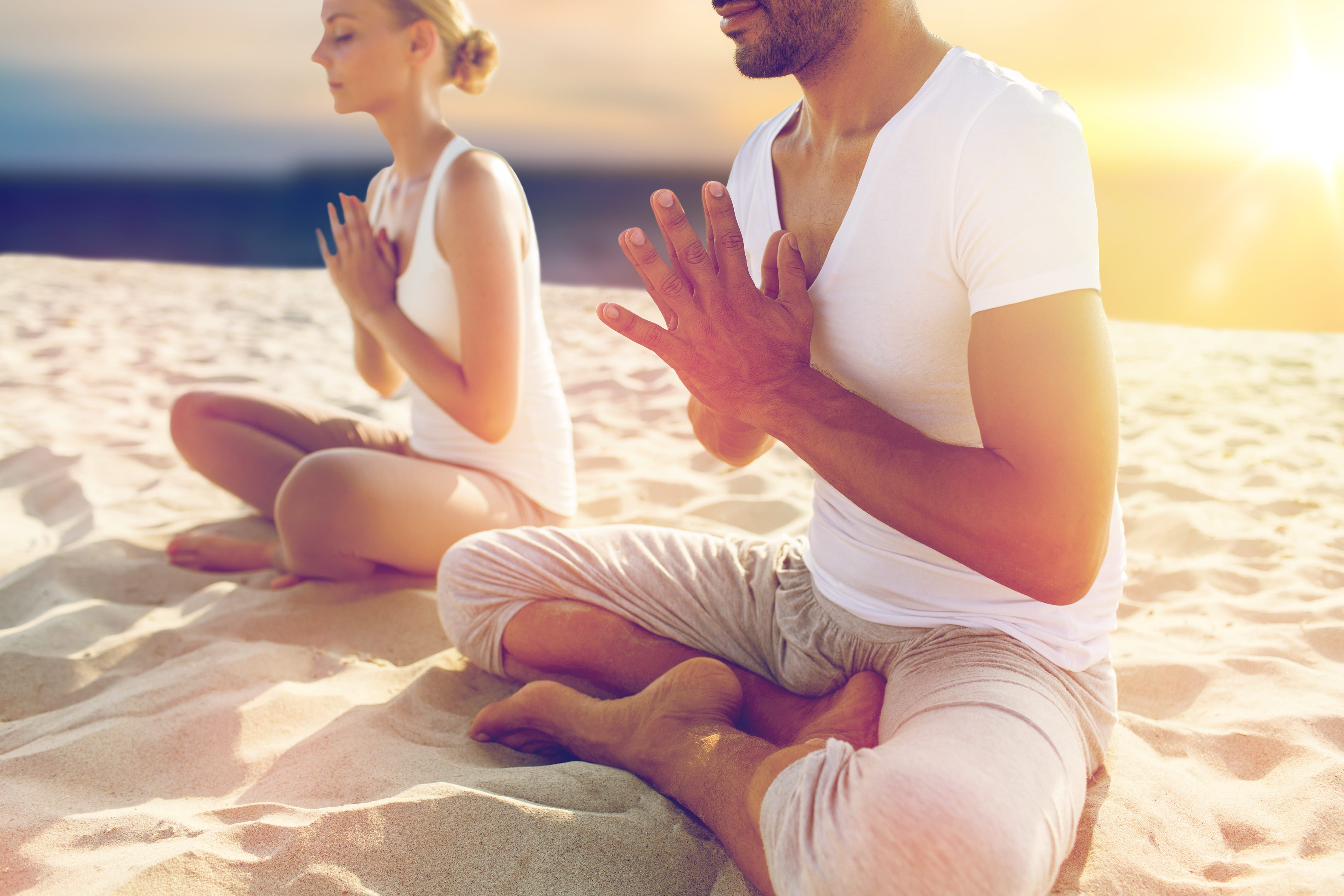 Couple meditating together on sandy beach during golden sunset hour