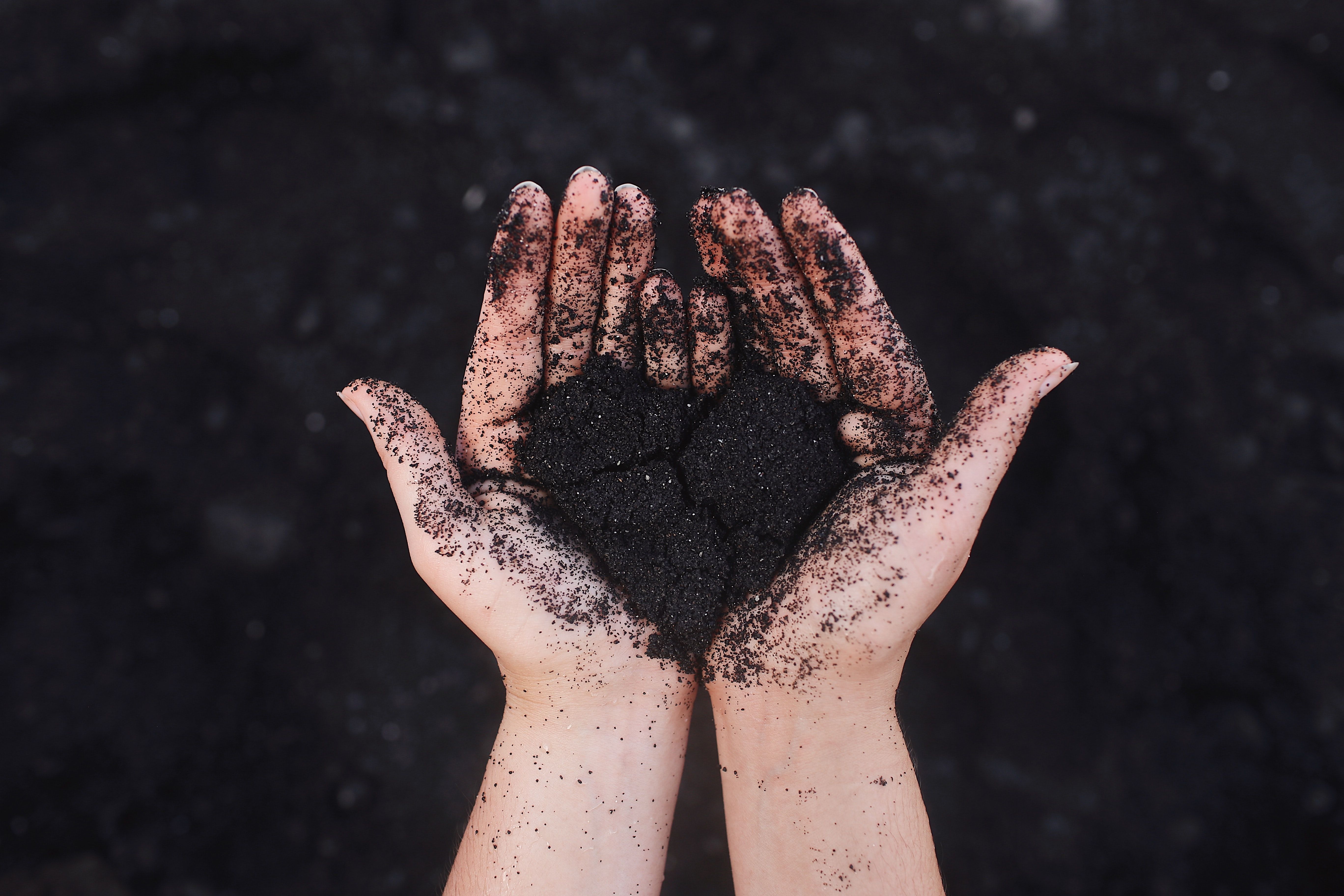 Open hands covered in black and bronze glitter against dark background